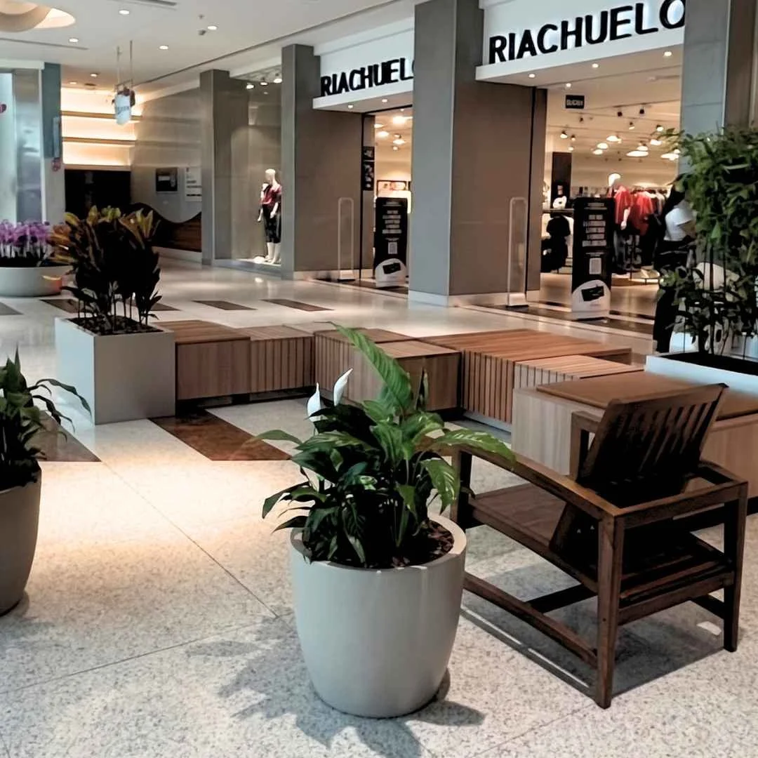 Área de permanência após a implantação parcial do retrofit, com mobiliário modular, vasos e vegetação integrados ao corredor do shopping center.