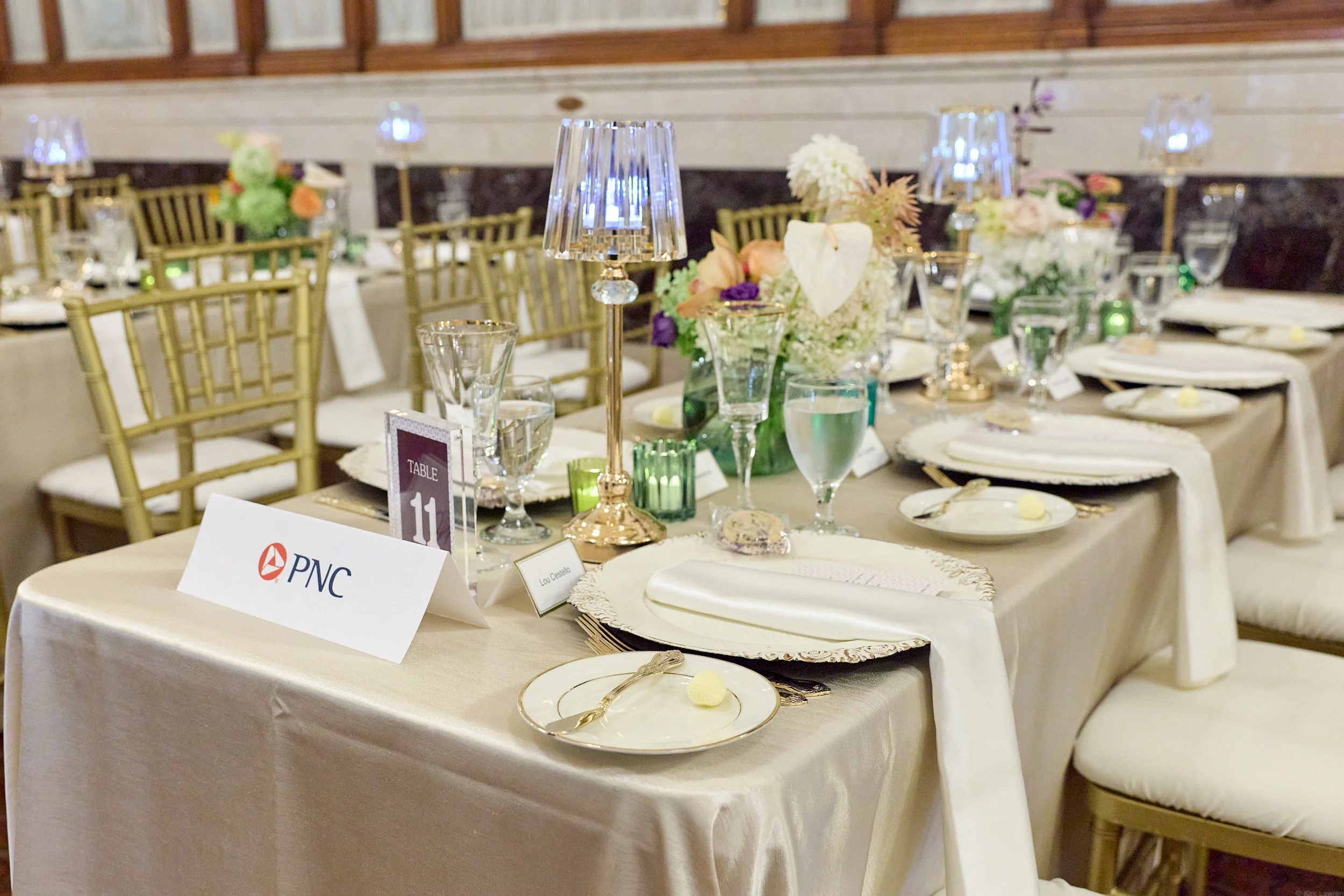 A banquet table decorated with floral centerpieces, glassware, and place settings, set up for a formal event or wedding reception.