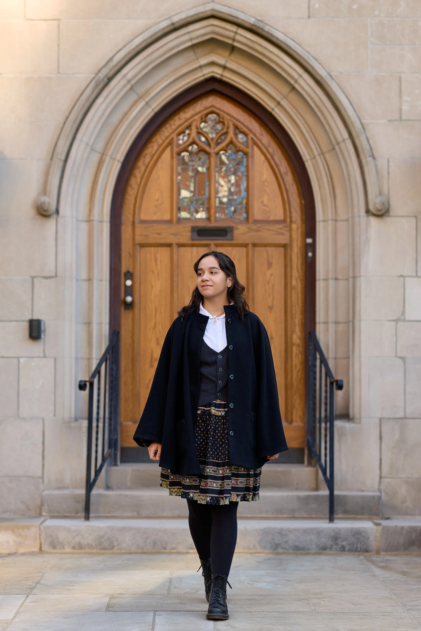 A young woman walking down stairs in front of a large wooden arched door with stained glass window at a church.