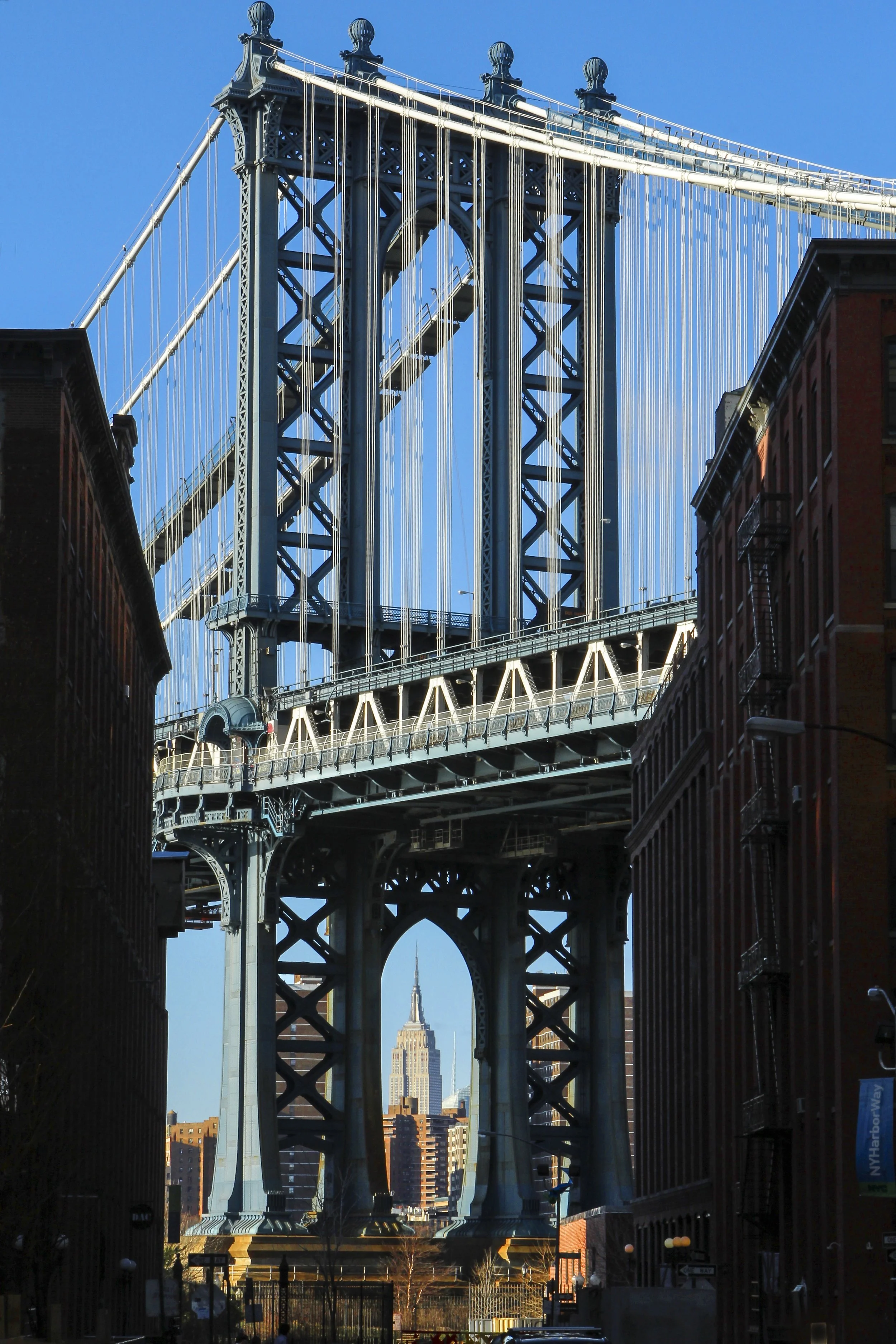 The image shows the Manhattan Bridge over a street in New York City with the Empire State Building visible in the background.
