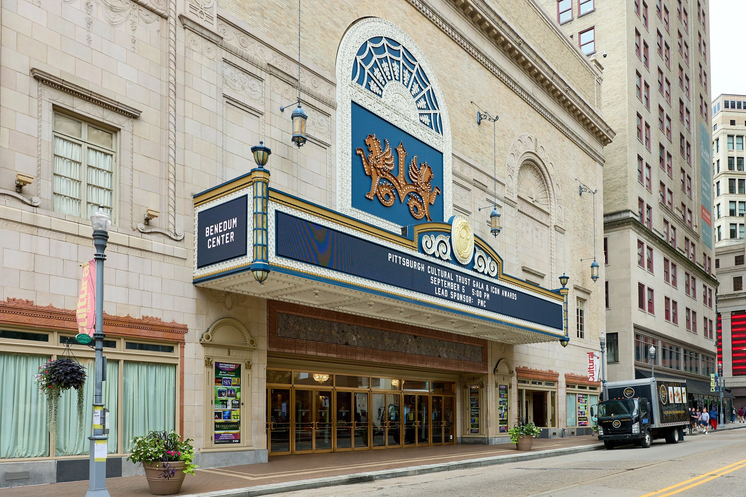 The exterior of the Benedum Center in downtown Pittsburgh, featuring a marquee with a blue background and gold accents, a lion crest, and decorative architectural details. The marquee displays information about the Pittsburgh Cultural Trust Gala and 
