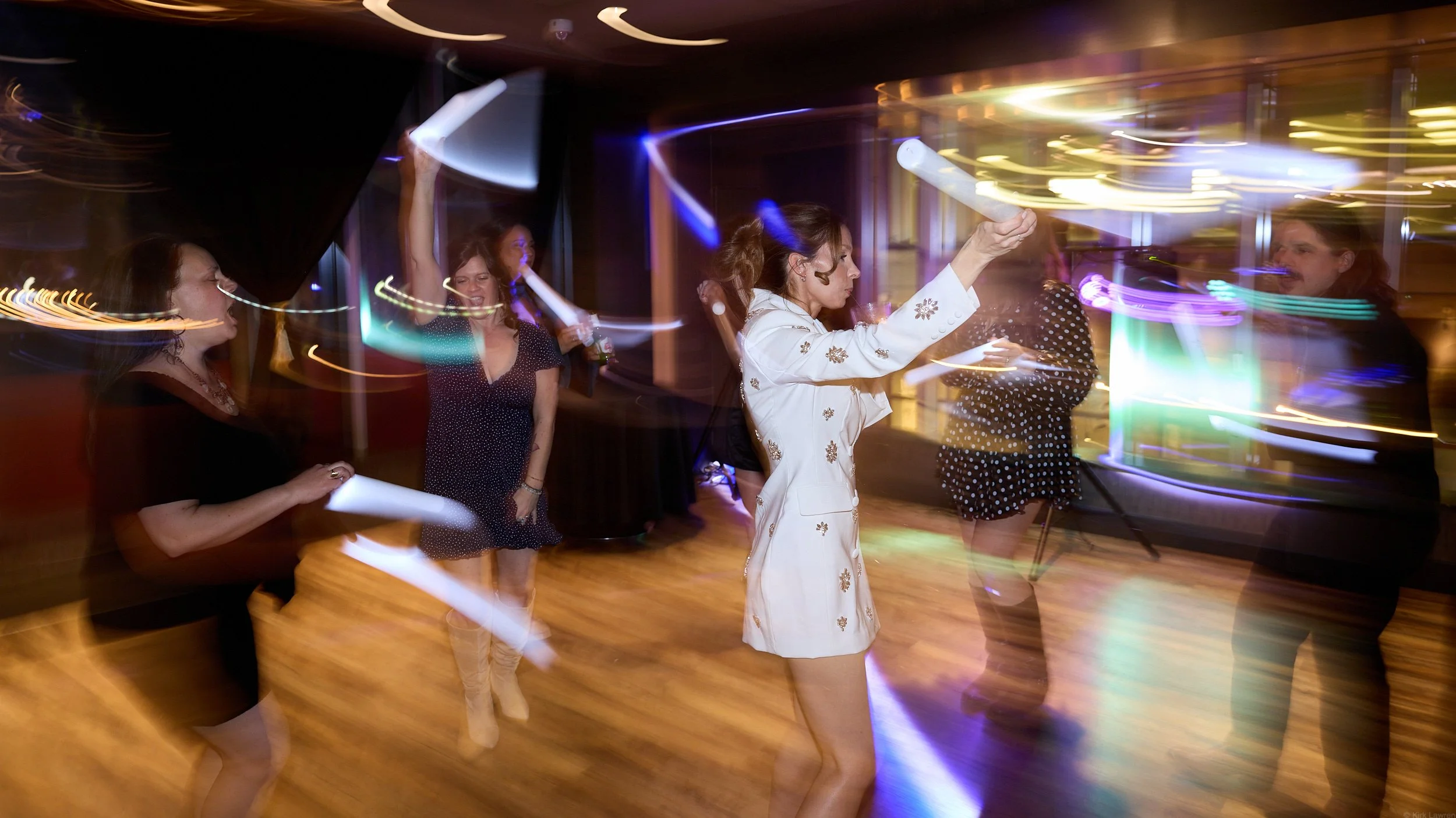 People dancing at a party with colorful lights and motion blur.