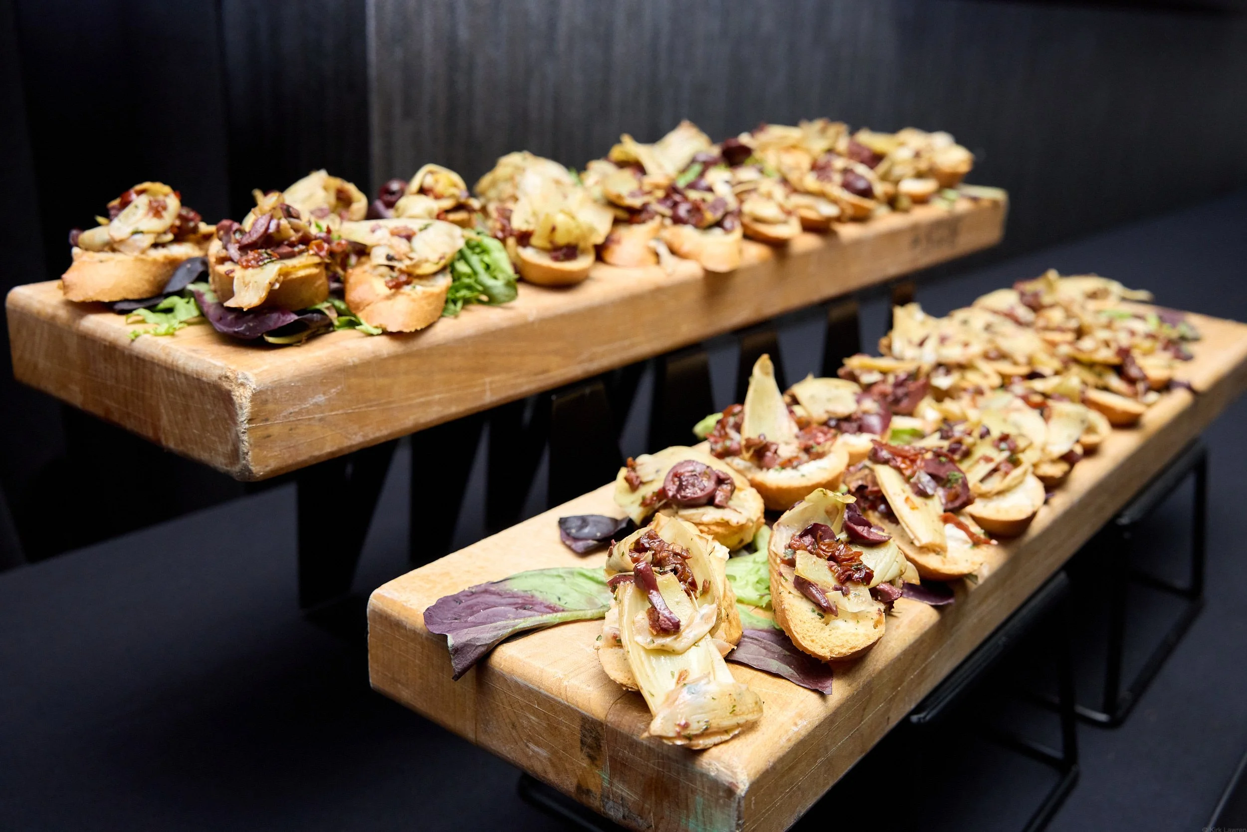 Wooden serving trays filled with assorted small bite appetizers topped with herbs and garnishes, displayed on a black surface with a dark background.