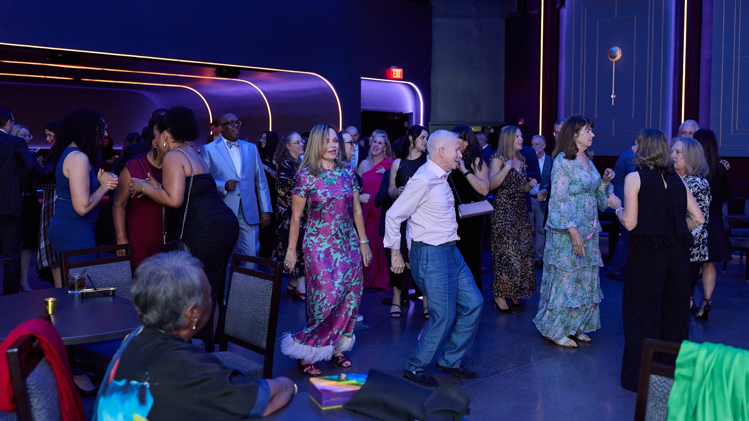 People dancing at a social event or party in a dimly lit room with blue lighting.