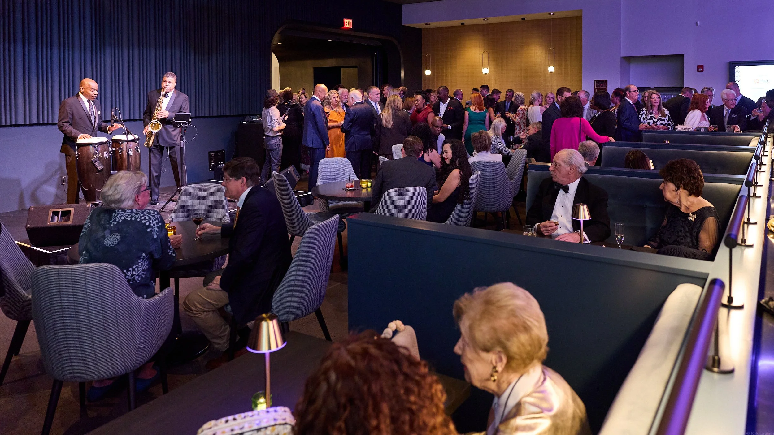 People dining and socializing at a formal event with a jazz band playing on stage.