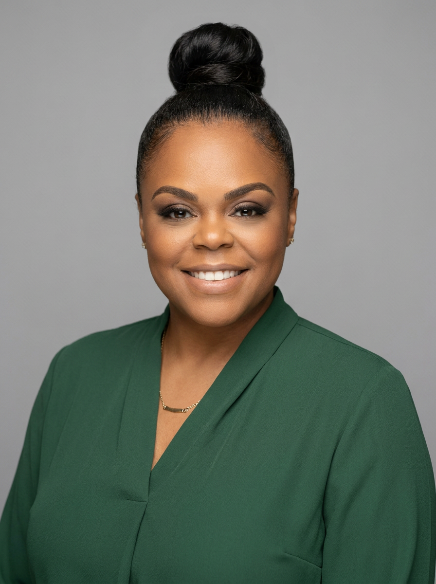 A portrait of a smiling African American woman with her hair in a high bun, wearing a green blazer, gold necklace, and small earrings, against a gray background.