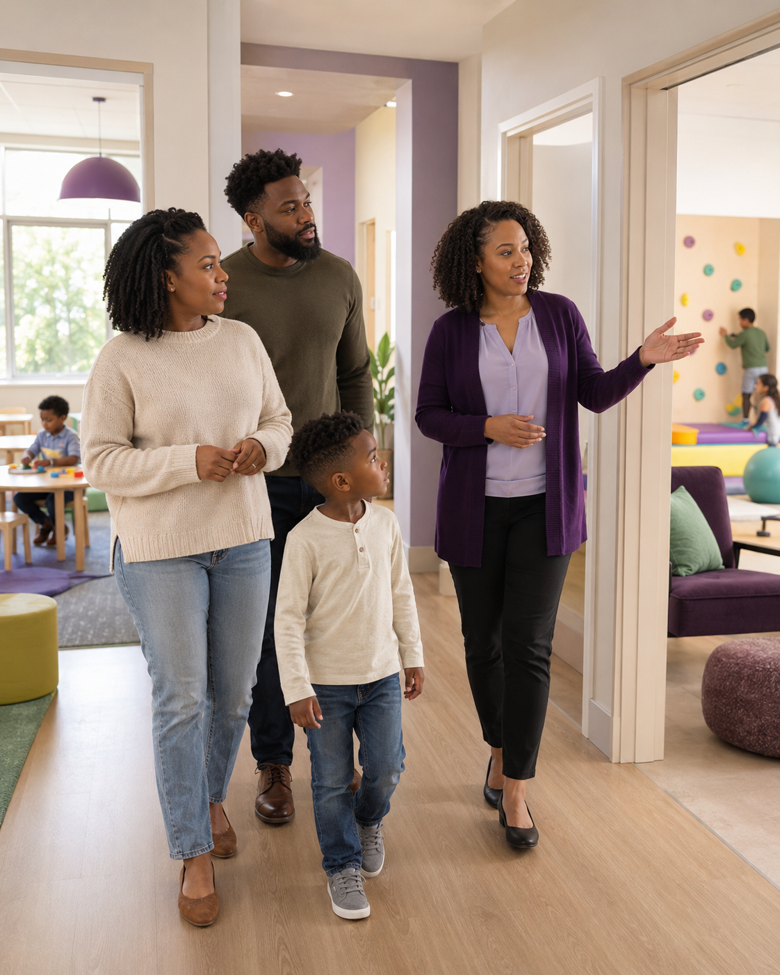 A group of four adults and one child walking through a colorful indoor play area, with a woman in a purple cardigan leading the way and children playing in the background.