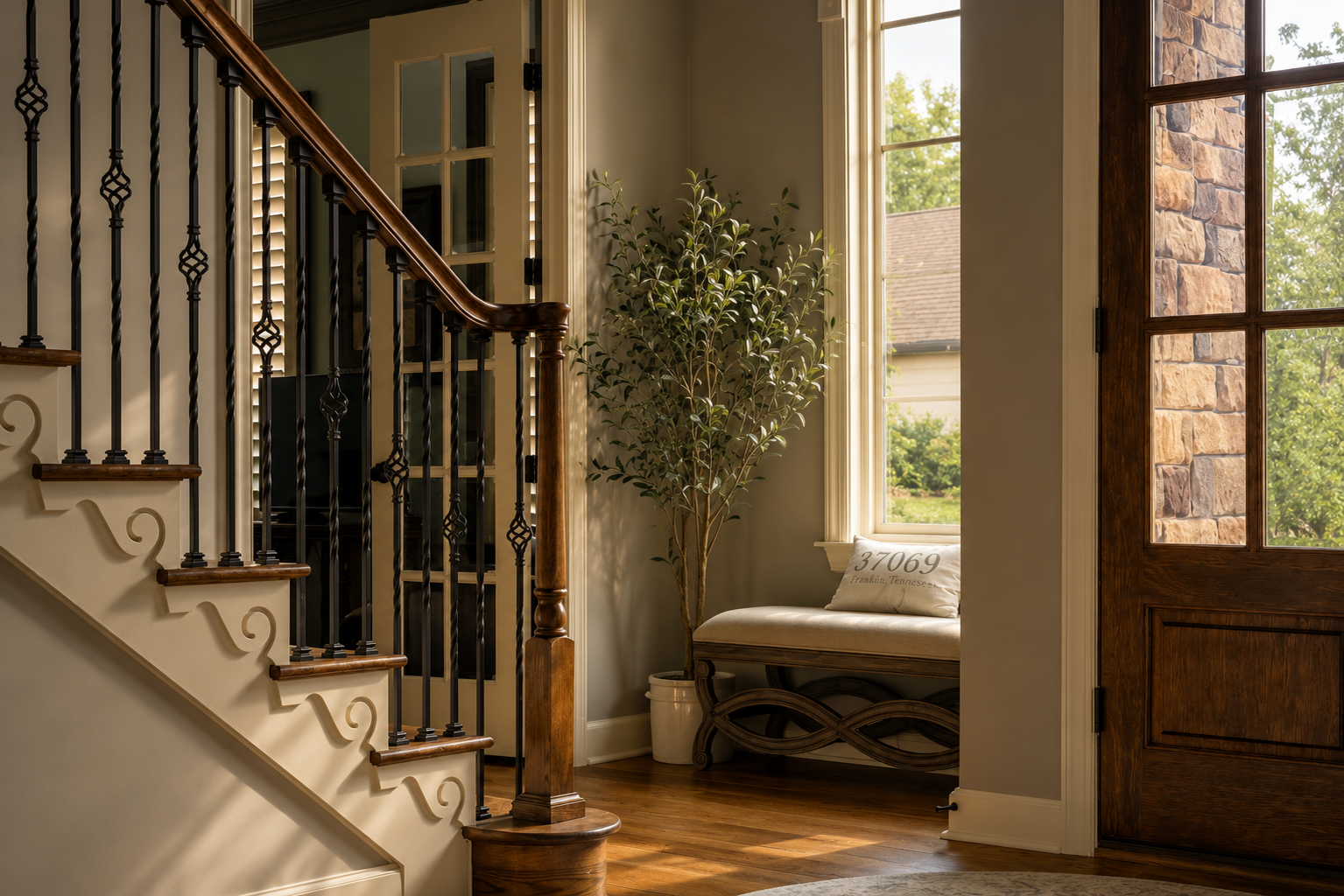 Entryway with a wooden front door, window seat with a pillow labeled '97069 Franklin, Tennessee,' potted plant, stairs with wooden handrail and black wrought iron balusters, and hardwood floors