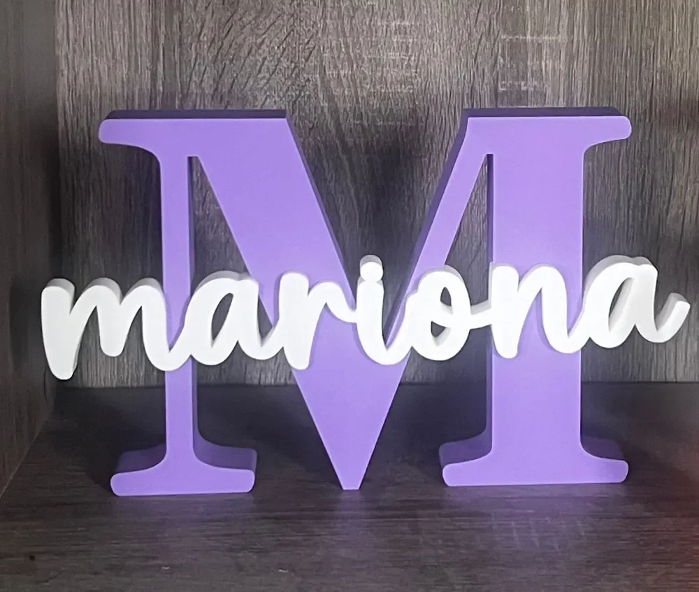 Decorative sign with a large purple letter 'M' and a white script word 'mariona' in front of a dark wooden background.