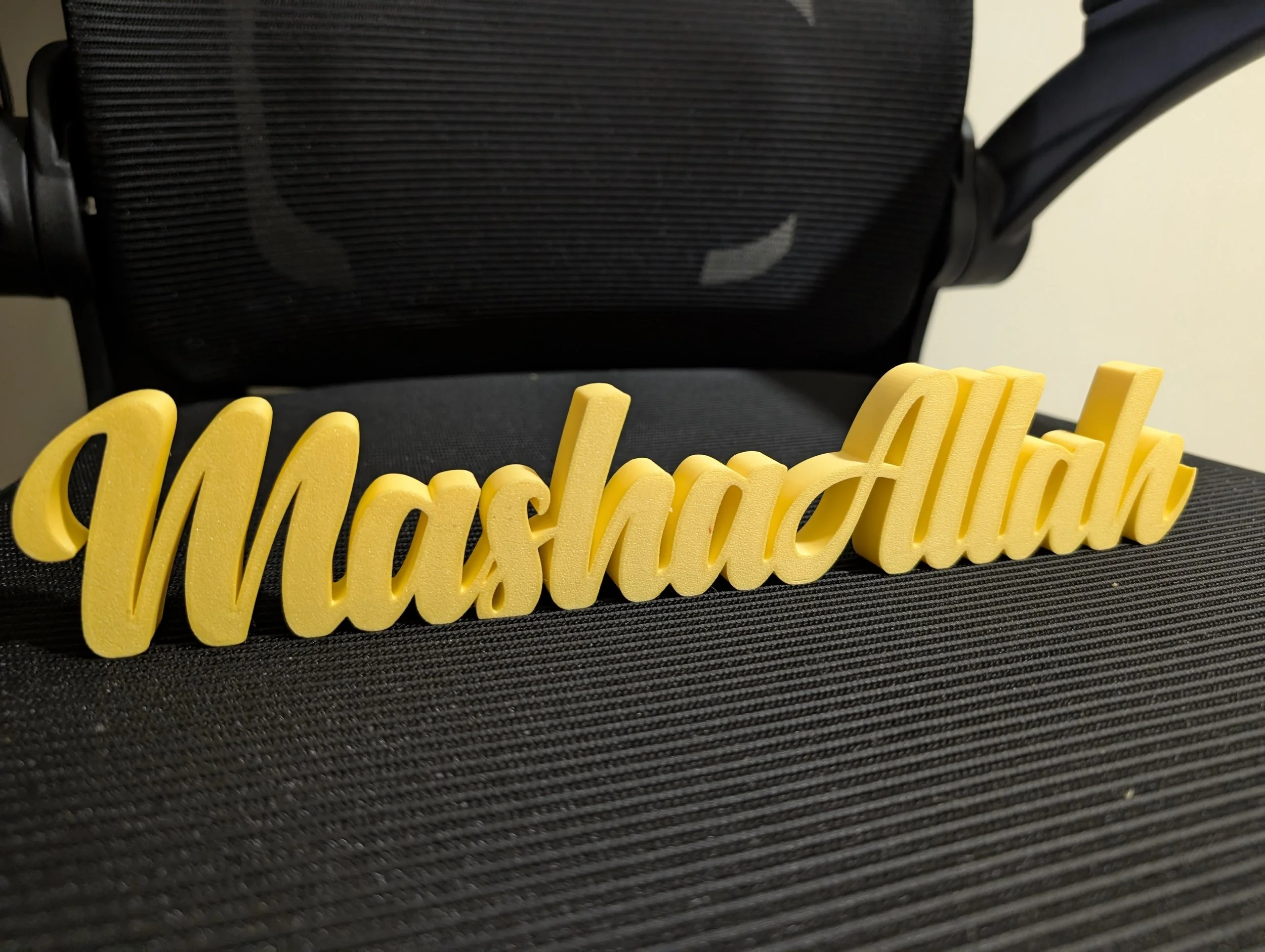Close-up of a yellow 3D sign spelling out 'Washington' placed on a black textured surface with a black mesh chair in the background.