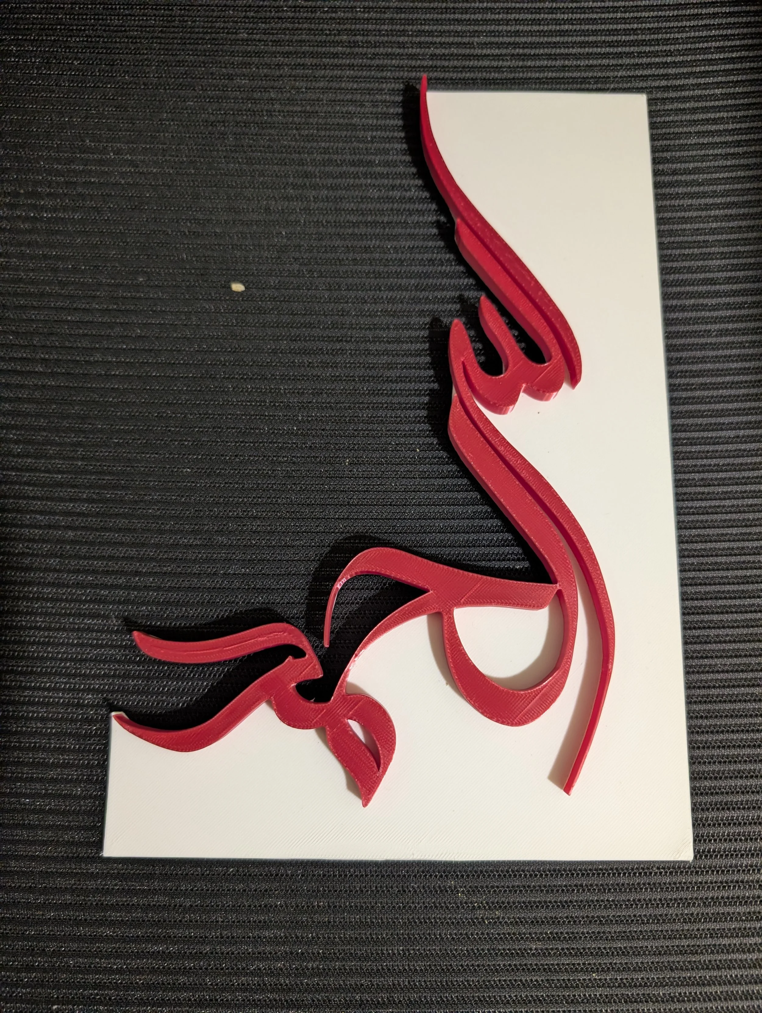 Red plastic flamingo cutout on white paper, on a black textured surface.