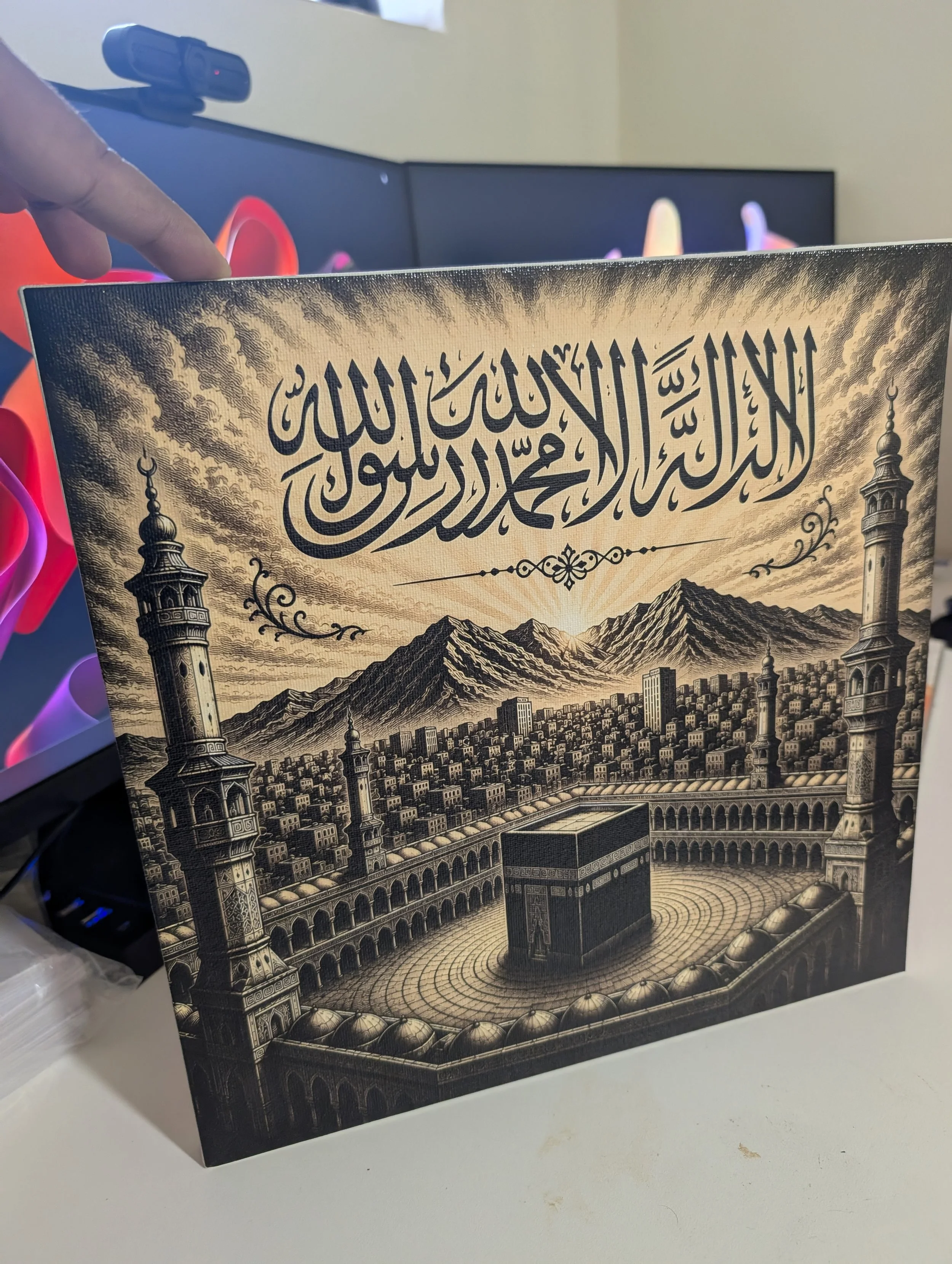 A decorative book with Islamic calligraphy and illustrations of mosque minarets and mountains on the cover, placed on a white desk.