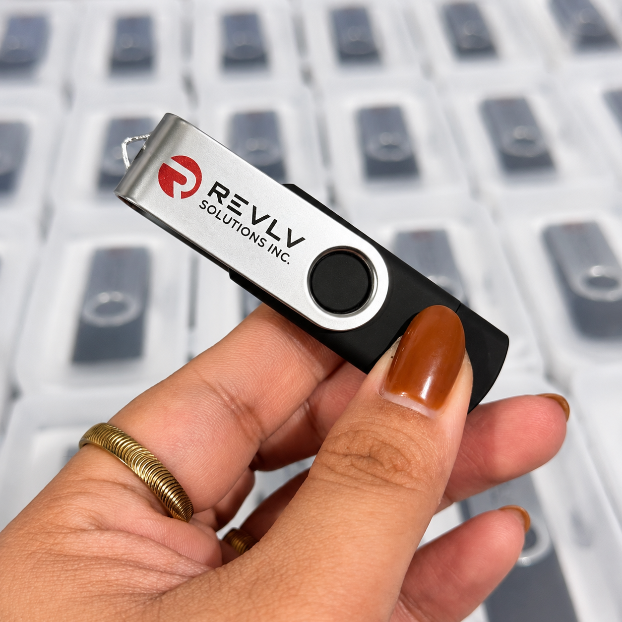 Close-up of a hand holding a USB flash drive with the label 'REVLV Solutions Inc.' against a blurred white keyboard background.