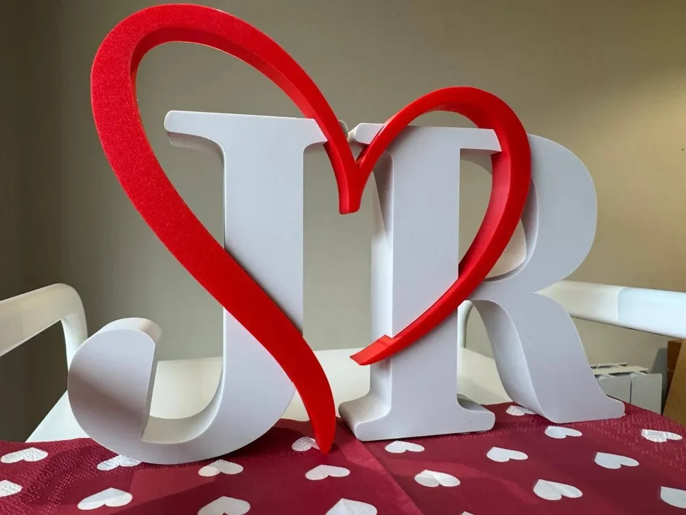 Decorative sign with white letters 'J' and 'R' connected by a red heart, placed on a table with a red heart-patterned cloth.
