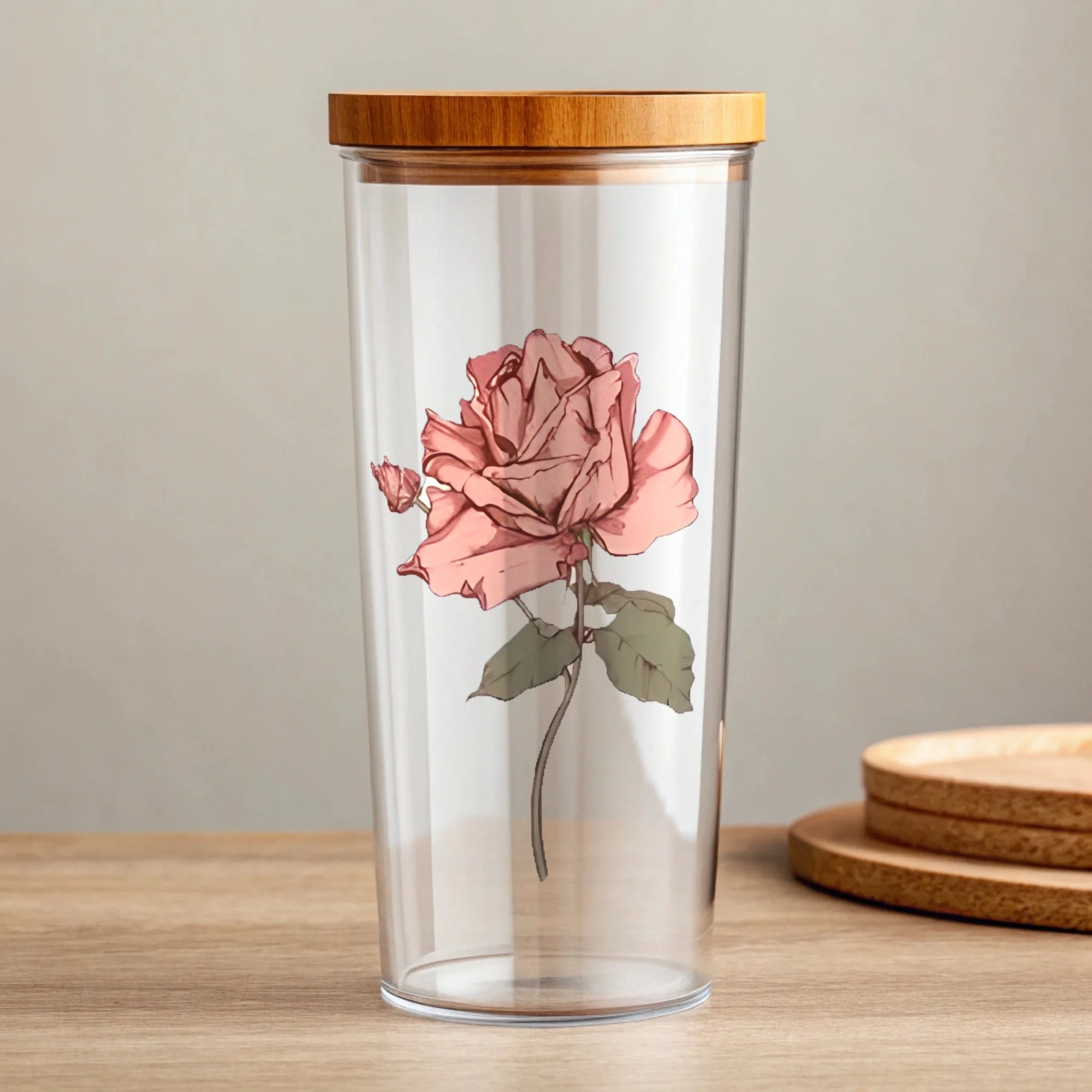 A cylindrical clear plastic container with a wooden lid, featuring a printed illustration of a pink blossoming flower on the front, placed on a wooden surface with two small stacked wooden dishes in the background.
