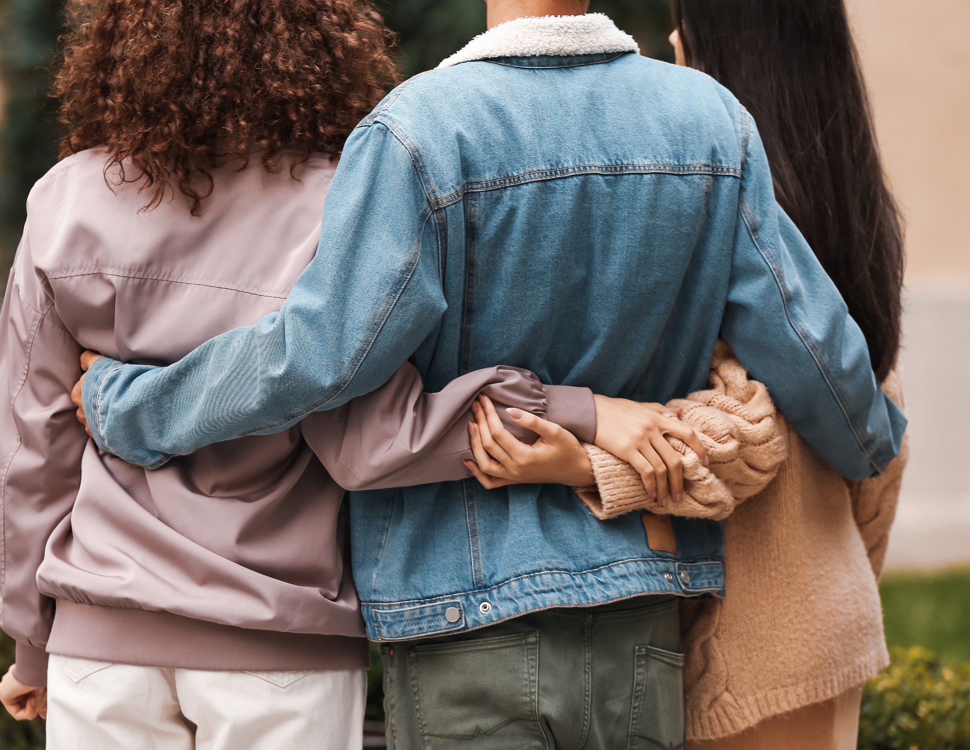 Three people stand, facing away from the camera, with their arms embracing each other