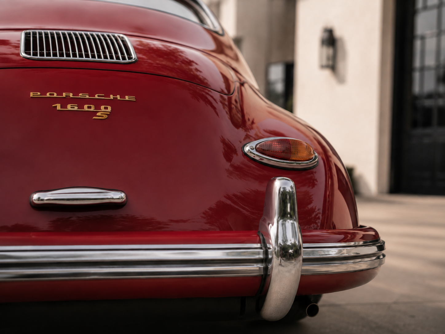 Close-up of the front of a red vintage Porsche 1600 S car with a chrome bumper and headlight, parked outside a building.