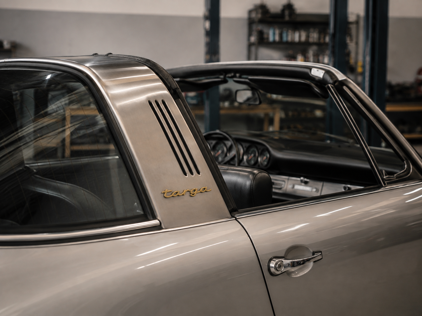 Close-up of a vintage Porsche Targa with silver exterior and black interior in a garage or workshop setting.