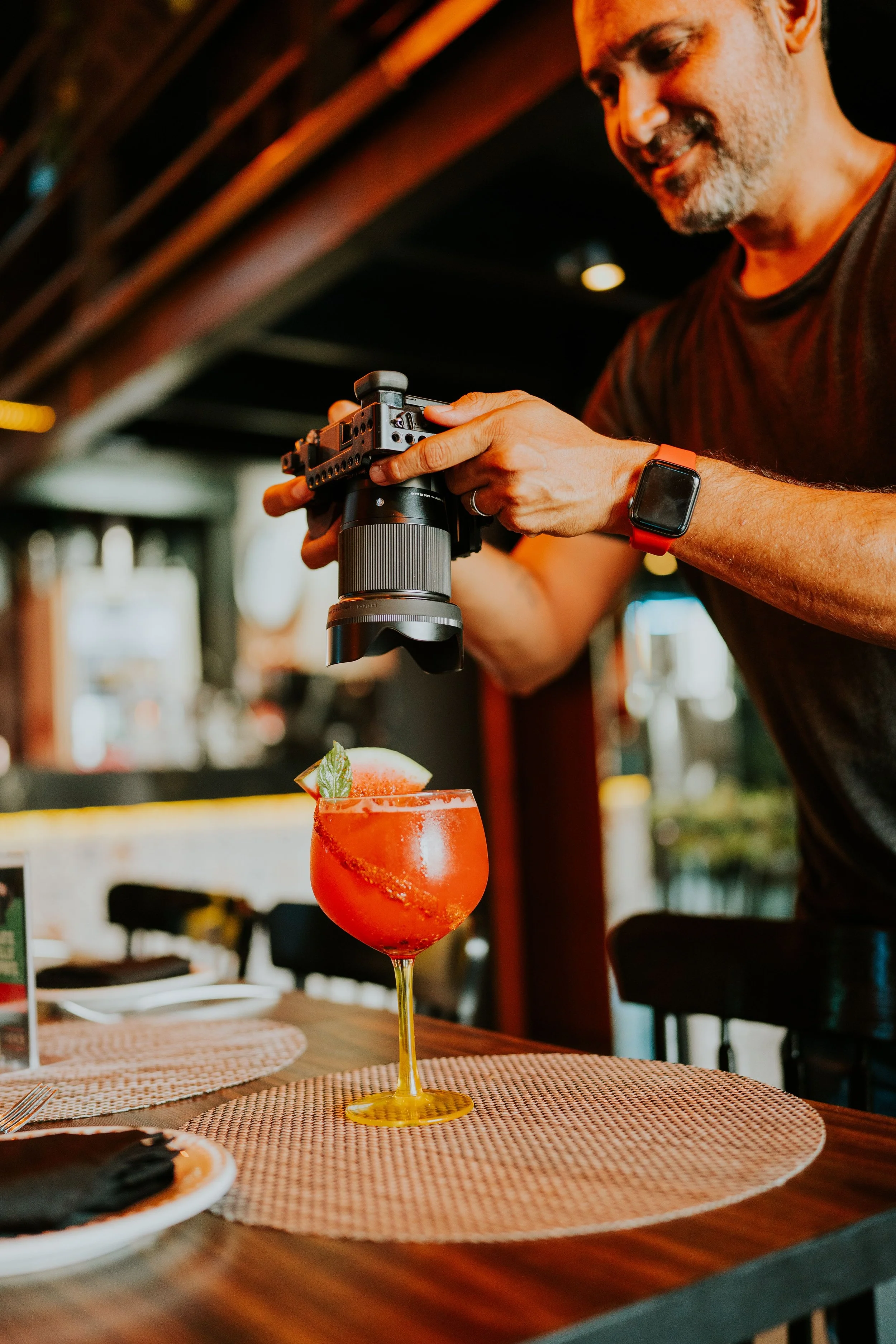 Hombre decorando un cóctel rojo en un restaurante o bar, con enfoque en la bebida y la mano que sostiene la cámara