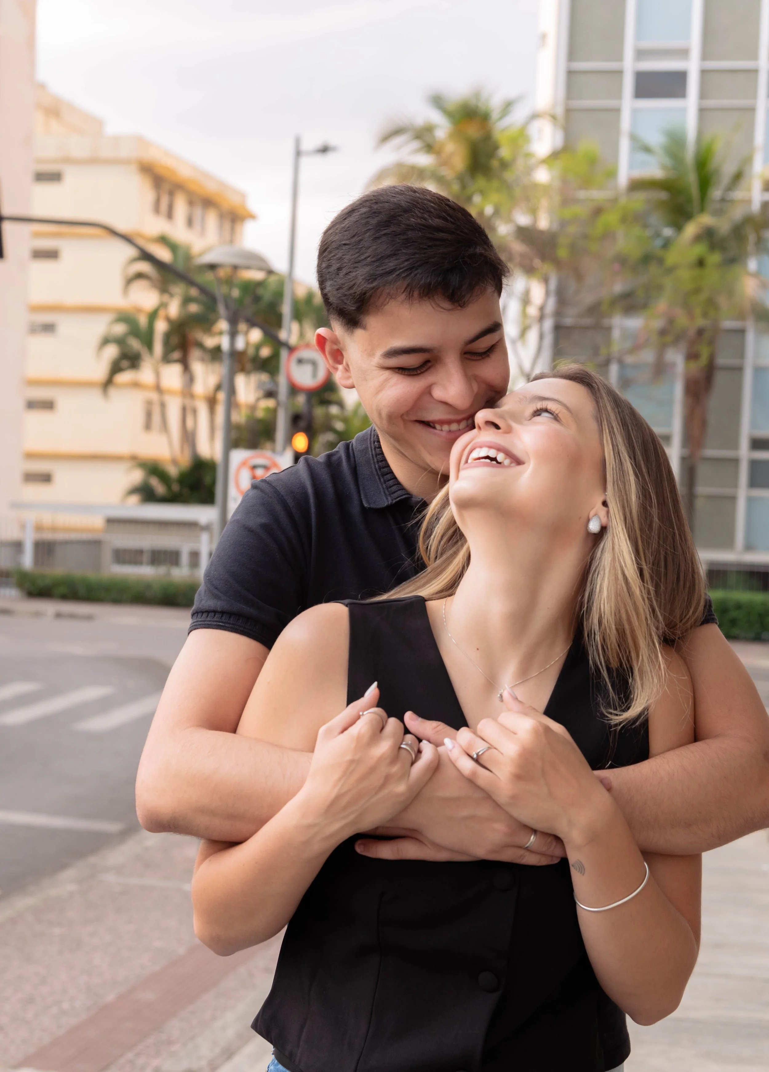 Una pareja comparte un abrazo en la calle, ambos sonríen y muestran afecto mutuo