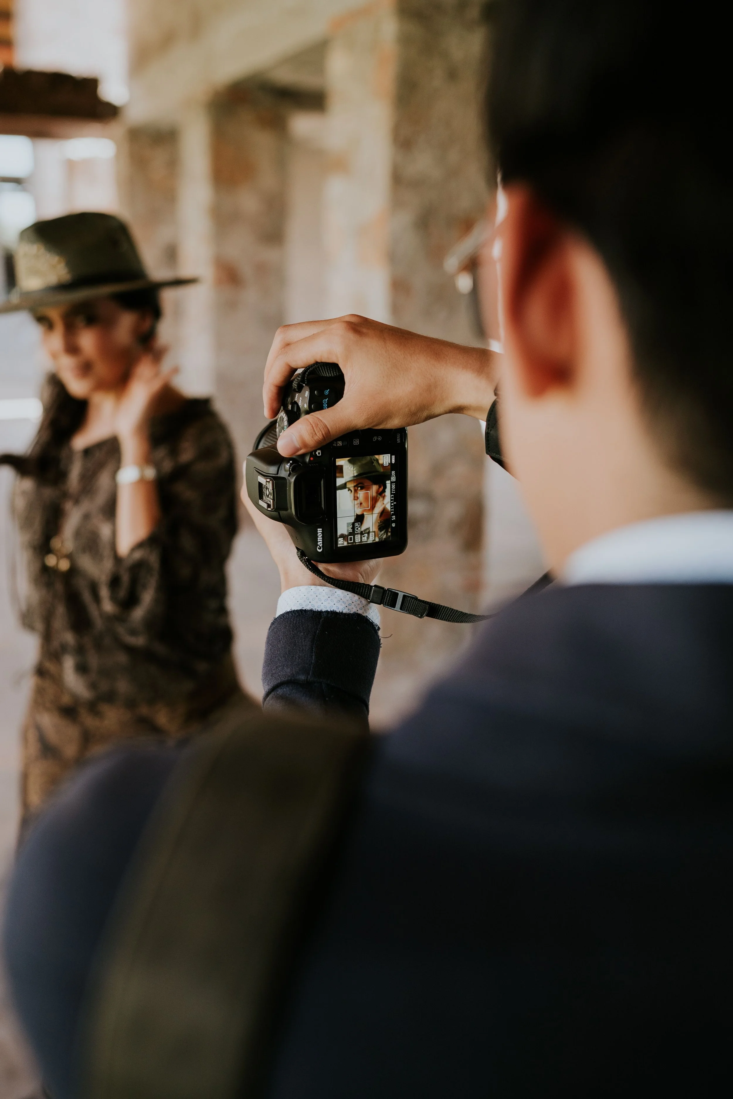 Persona tomando una fotografía de una mujer vestida con ropa de estampado animal print y gorra, en un espacio con paredes de ladrillos expuestos.