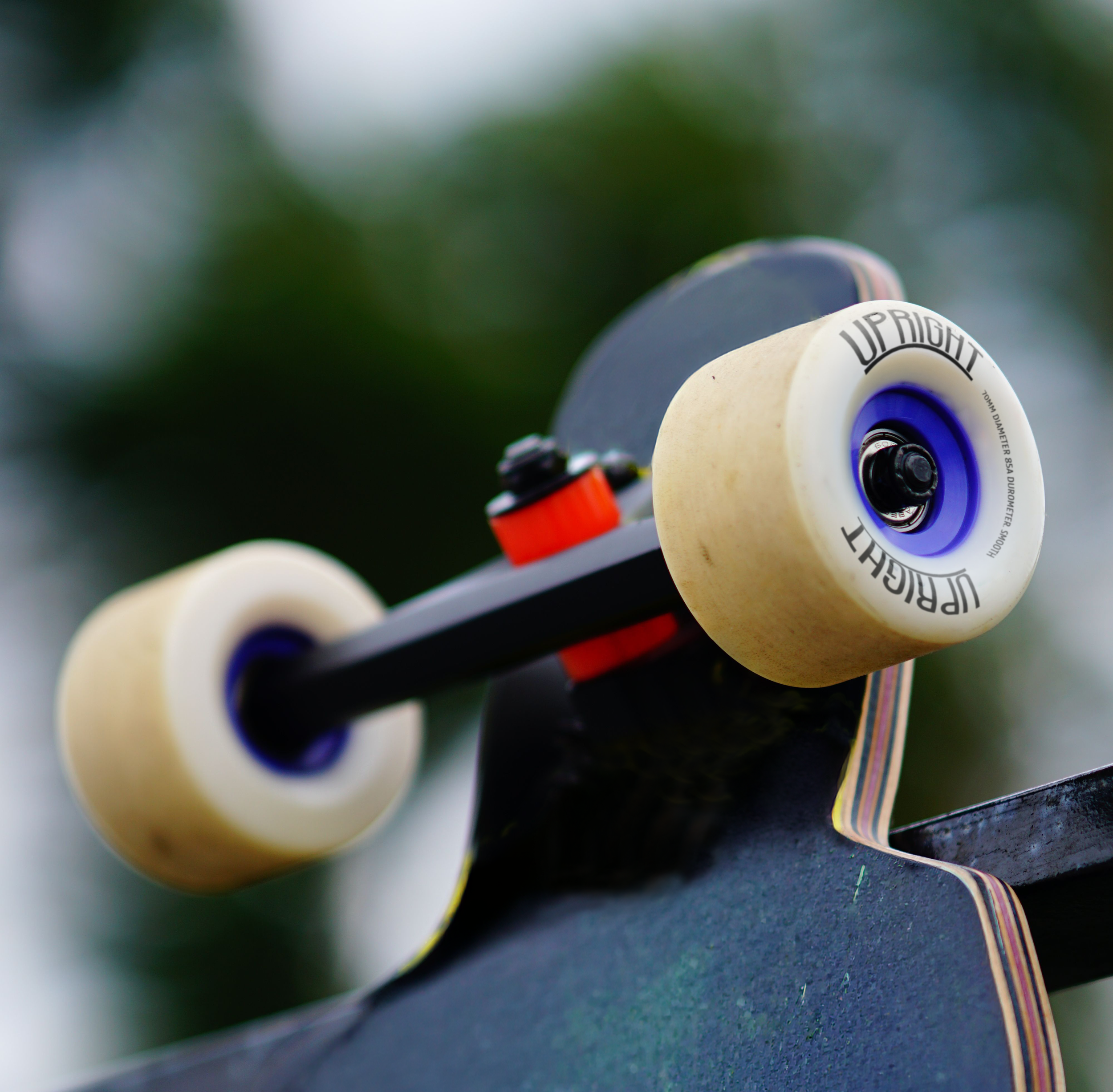 Close-up of skateboard wheels with the word 'UPRIGHT' printed on the side, set against a blurred outdoor background.