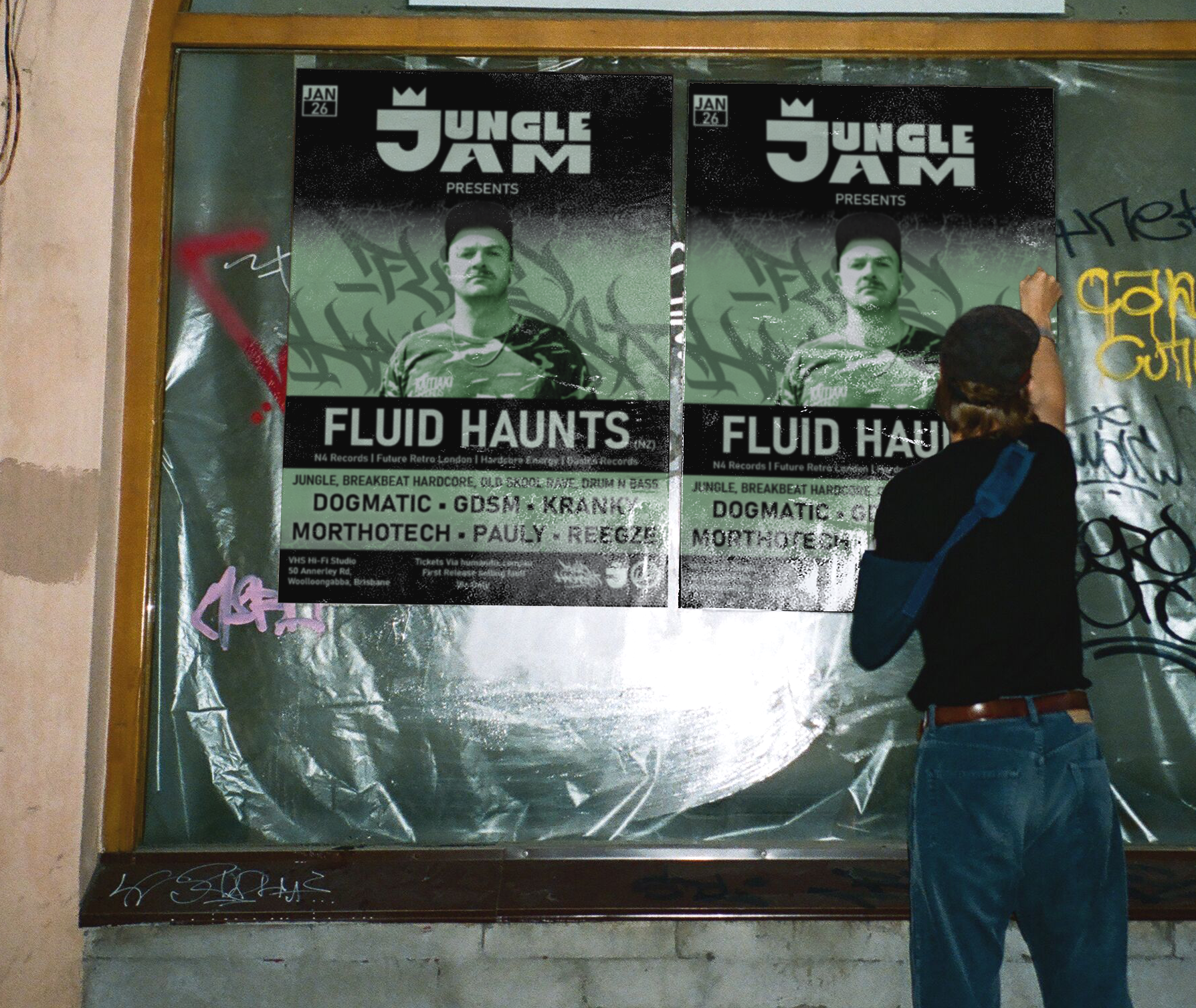 A person with brown hair, wearing a black cap, a black T-shirt, and blue jeans, is writing or drawing on a graffiti-covered wall next to a large poster for 'Jungle Jam Presents Fluid Haunts' concert, featuring a man with a mustache, wearing a black hat.