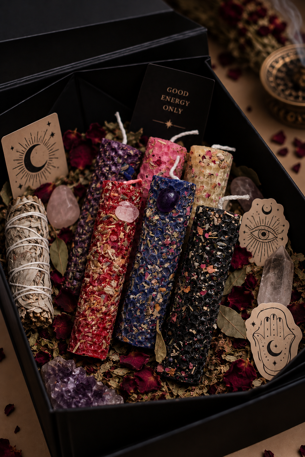 Colorful candles with dried flower petals and crystals in a black gift box, decorated with celestial and eye-themed stickers.