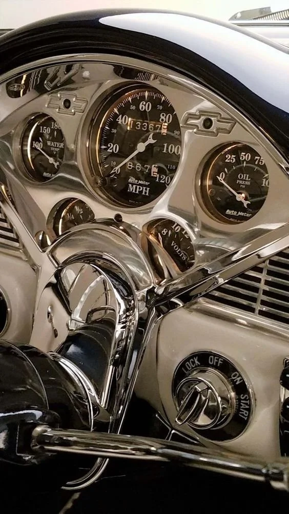 Close-up of a vintage car dashboard with speedometer, water temperature, oil pressure, and voltmeter gauges, and a steering wheel.