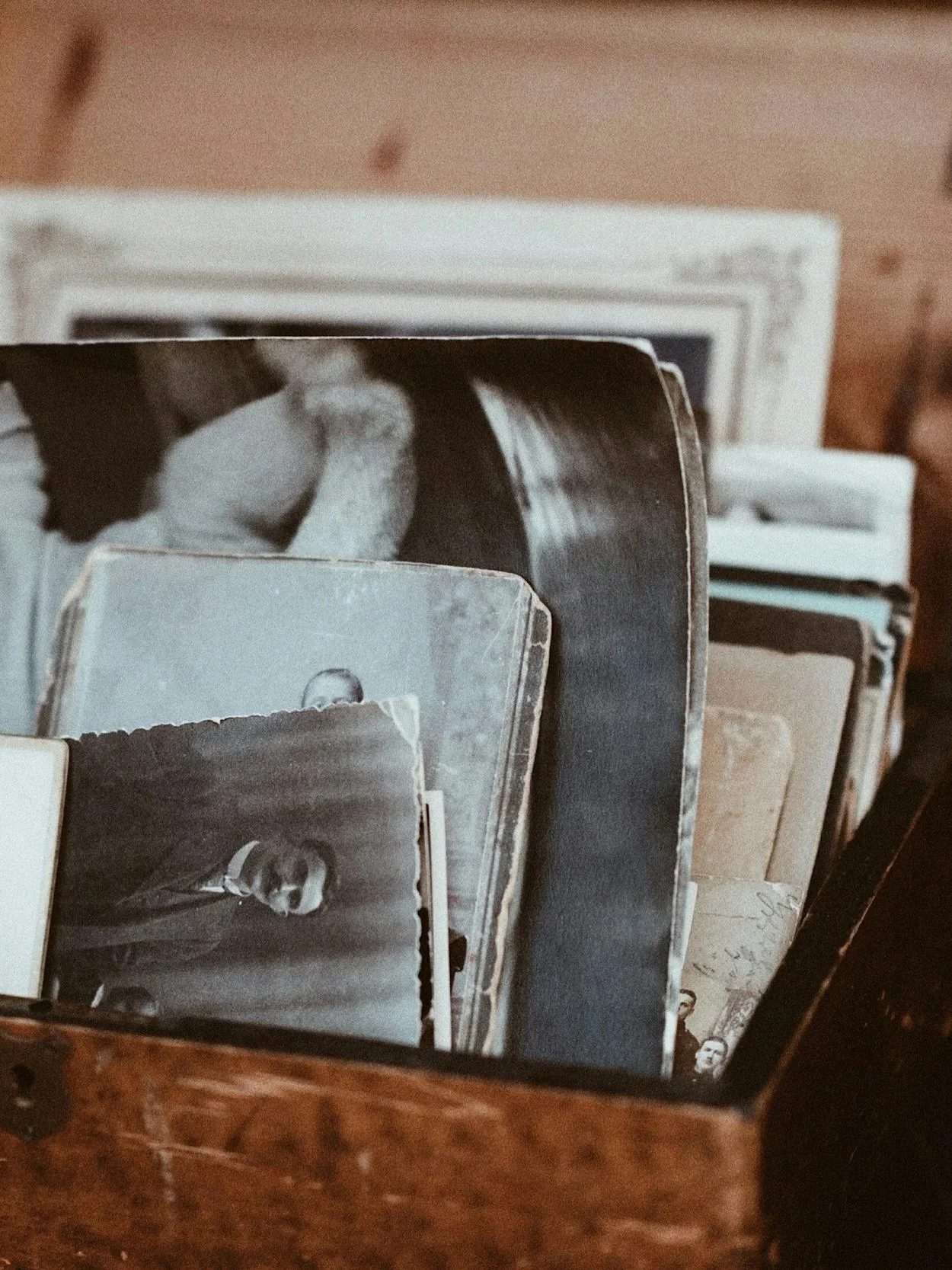 A collection of black-and-white photographs, some of which are torn around the edges, displayed upright in a wooden box. The photos depict various individuals, possibly historical or vintage images.