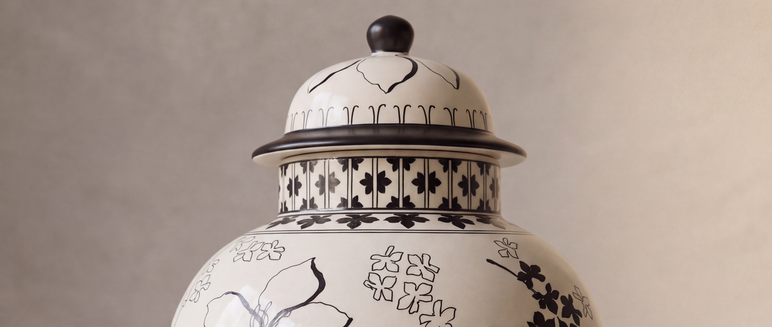 Close-up of a decorative ceramic jar with floral and line patterns in black on a white background, featuring a rounded lid with a black knob.