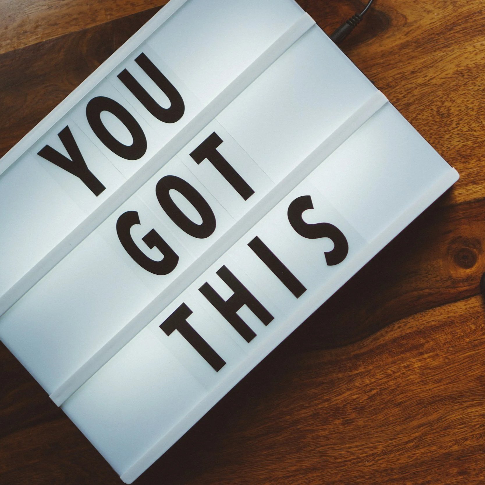 A lightbox sign with black letters on white panels spelling out 'You Got The Job' on a wooden surface.