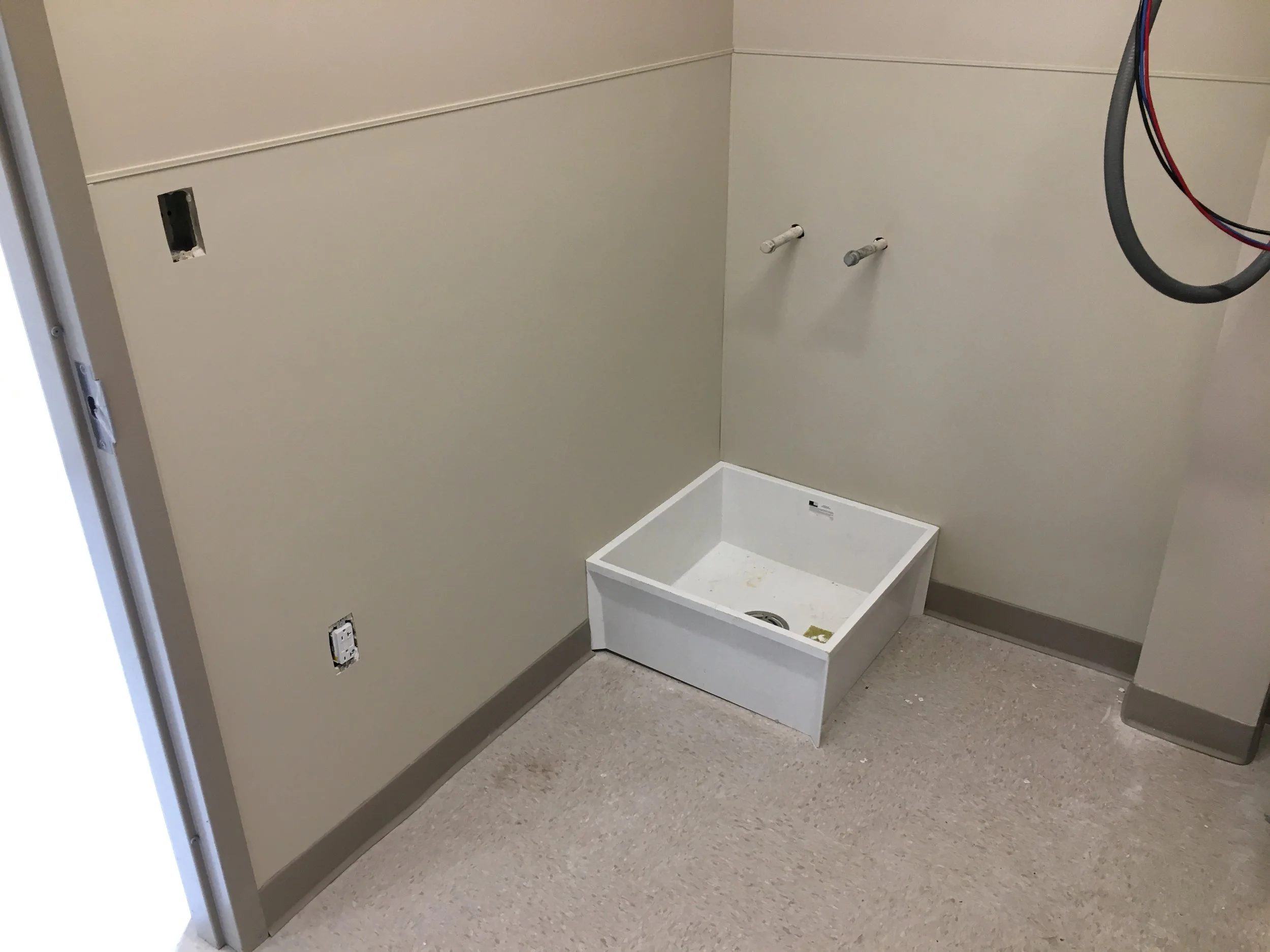 Unfinished laundry room with empty washer and dryer hookups, a laundry sink, and electrical outlets on the wall.