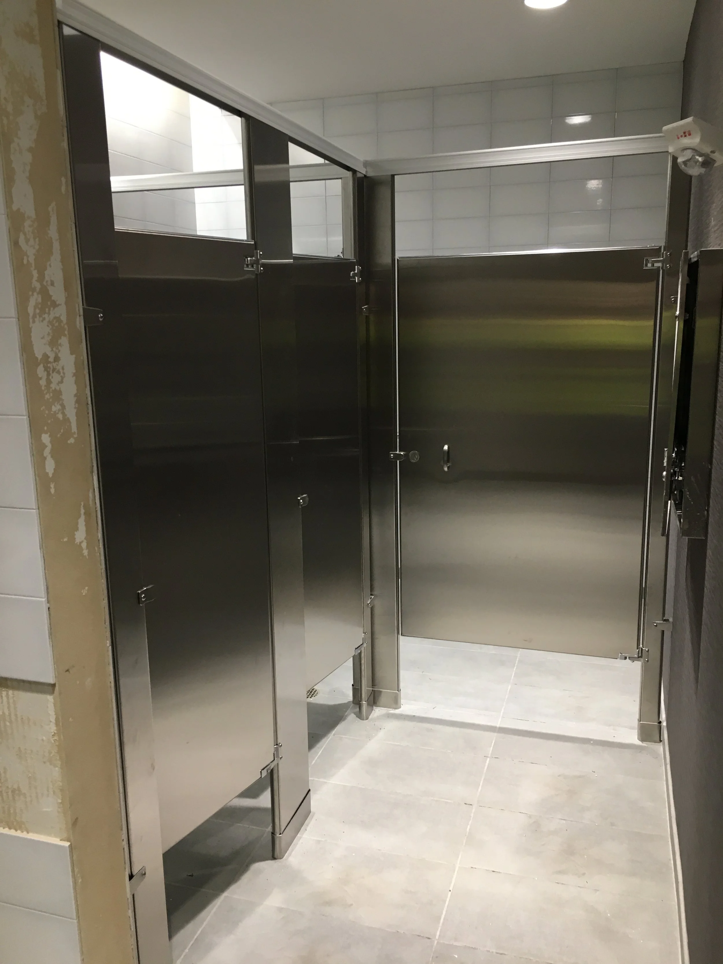 Empty public restroom with stainless steel toilet stalls and tiled floor.