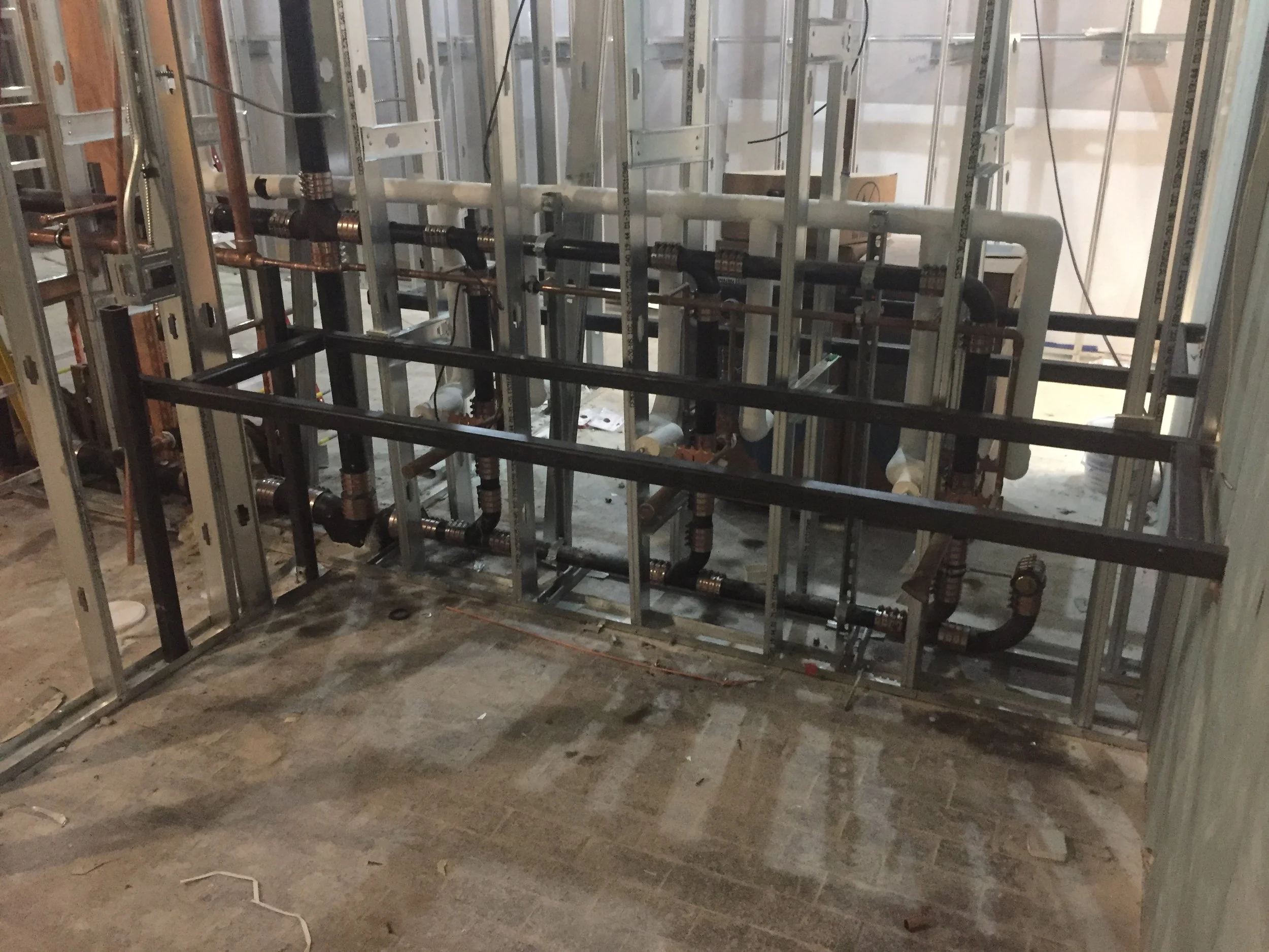 Construction site with metal framing and plumbing pipes installed, unfinished interior walls.