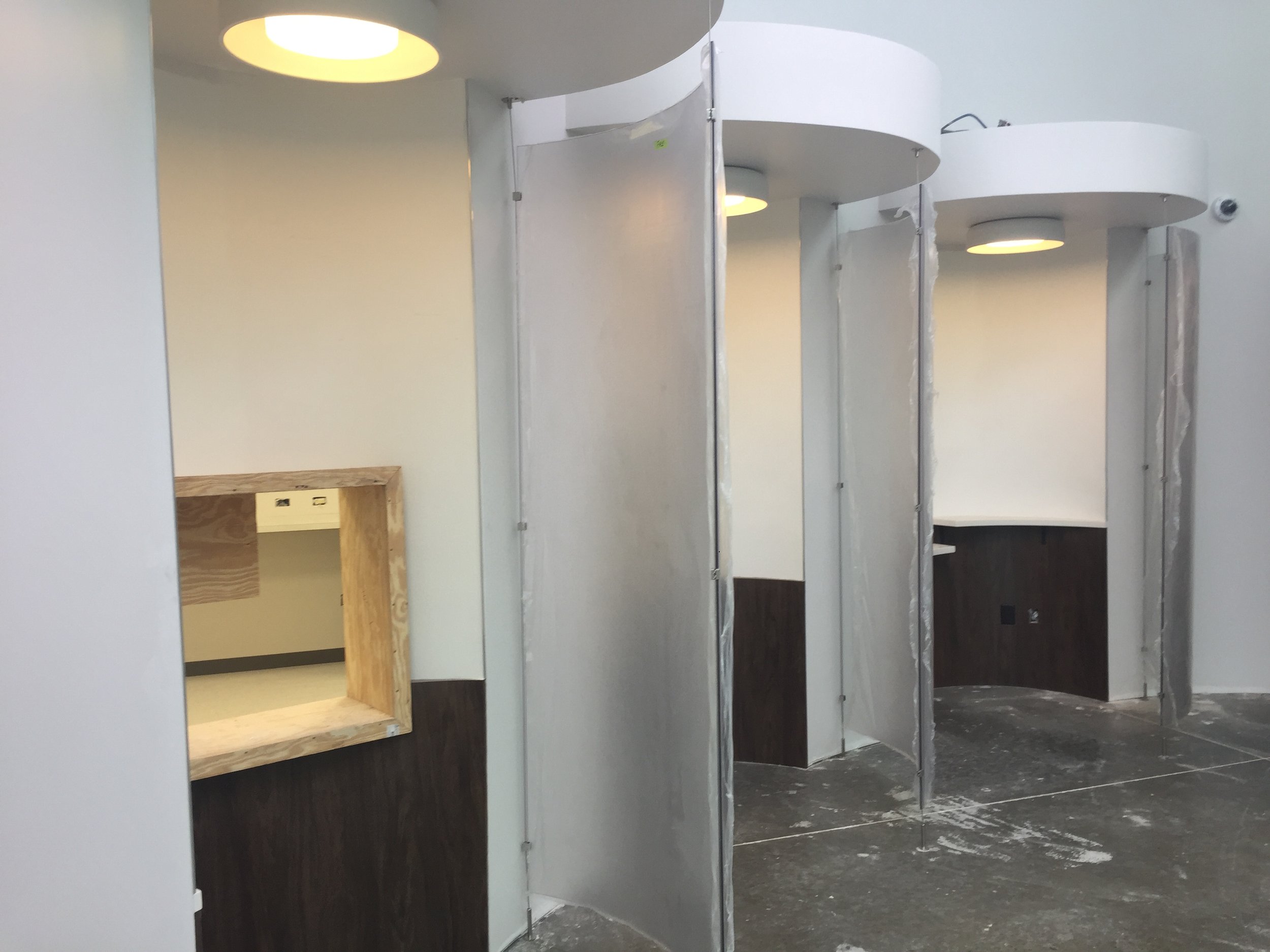 Partial view of modern, curved restroom stalls during construction or renovation, with some areas showing unfinished surfaces and exposed hardware.