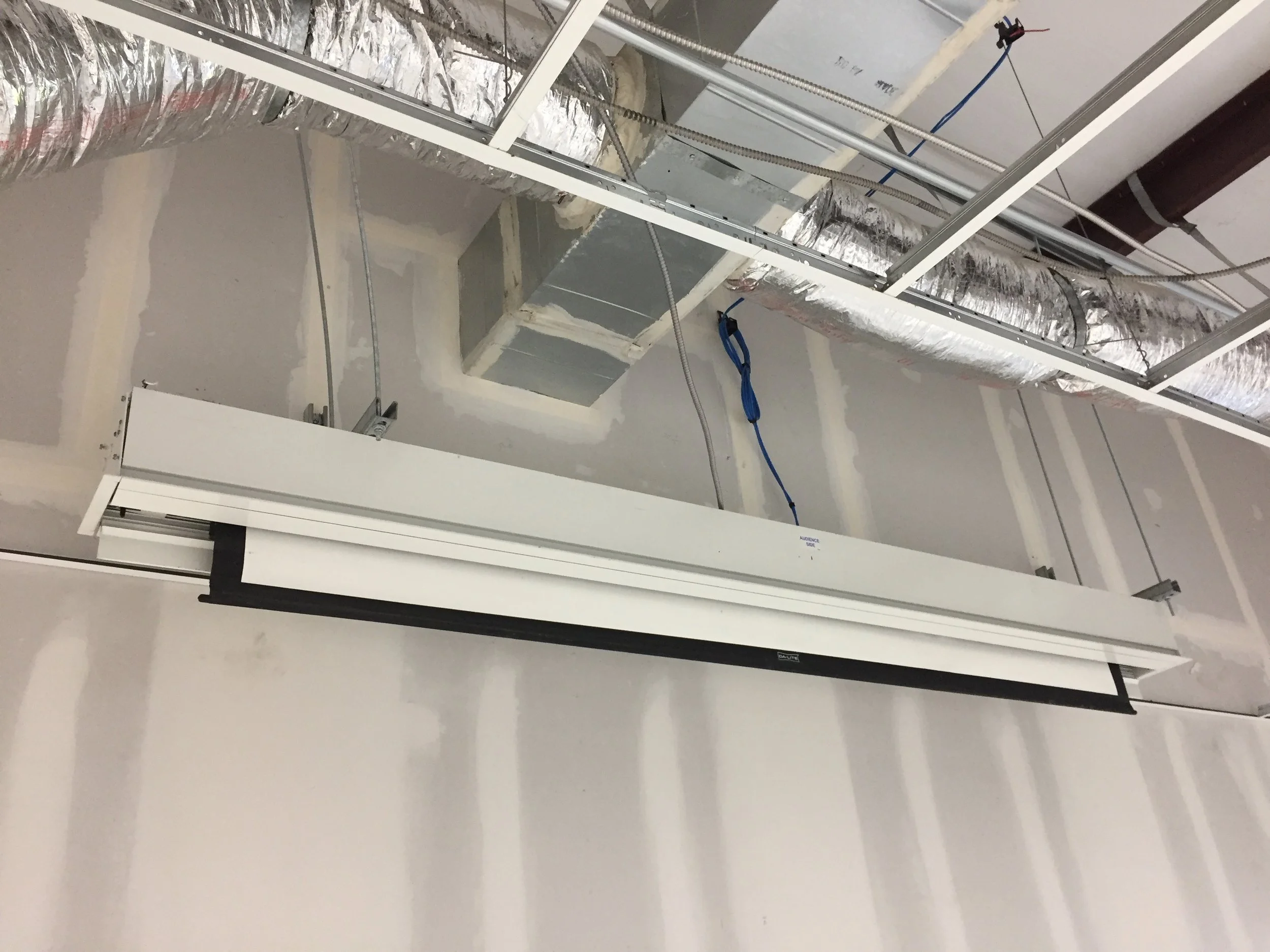 Construction site with metal framework, insulated air ducts, and electrical wiring in progress, ceiling partially unfinished.