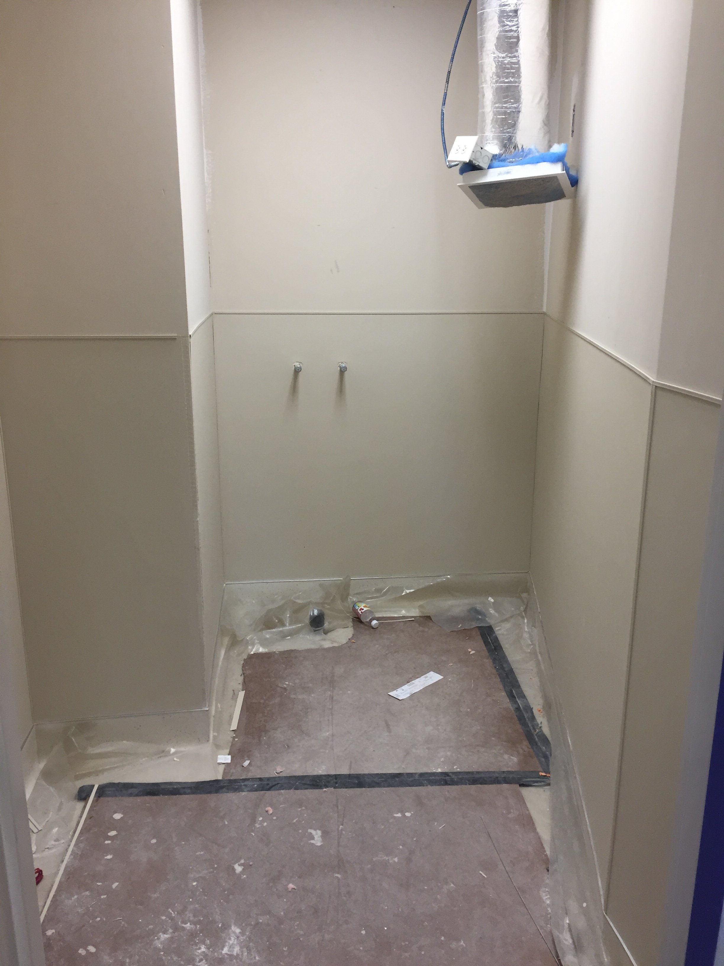 Empty elevator with some construction debris on the floor, plastic sheeting on the floor, and uncovered ventilation ductwork.
