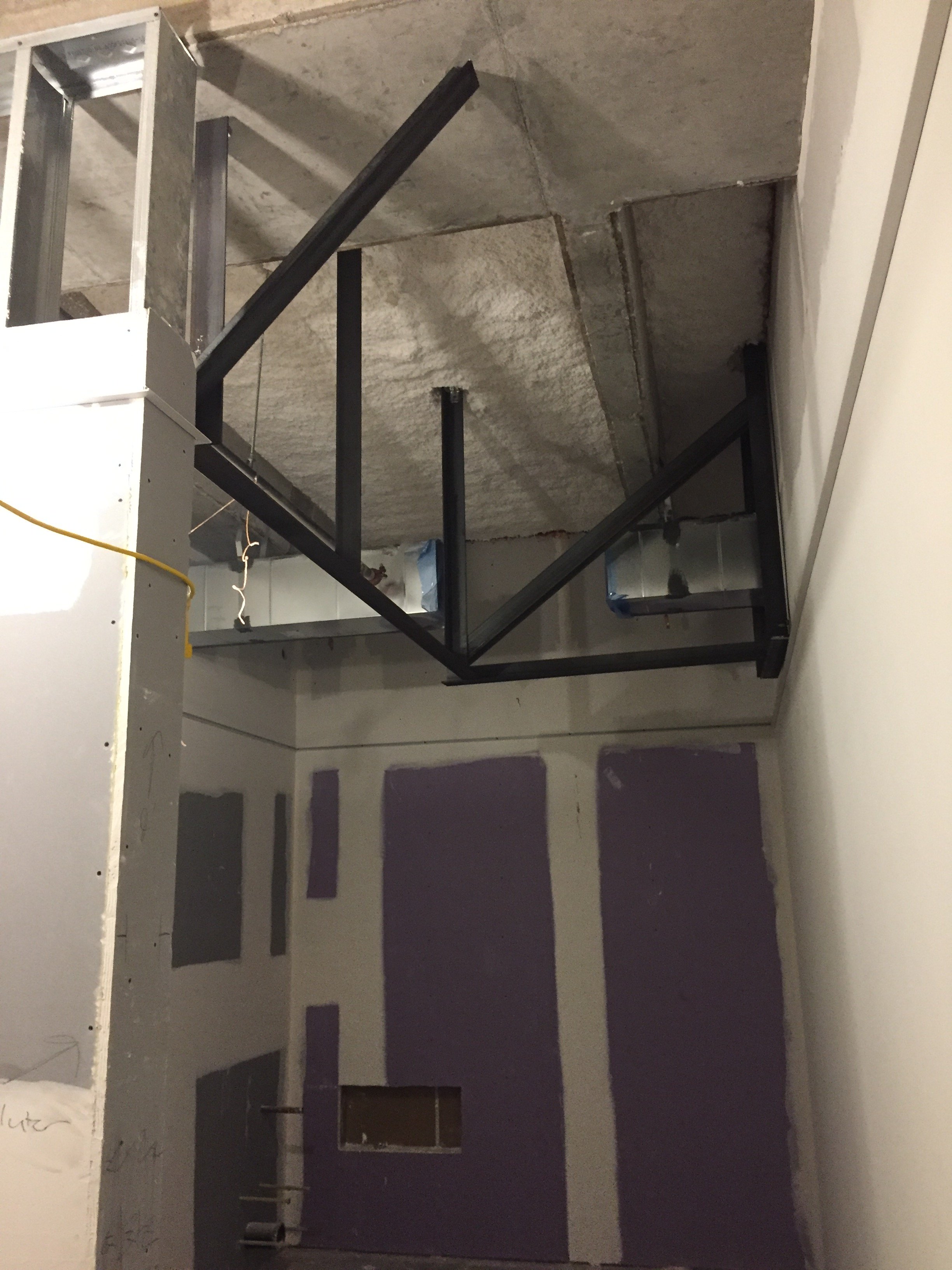 Building under construction with metal framing, drywall, exposed pipes, and an unfinished ceiling.