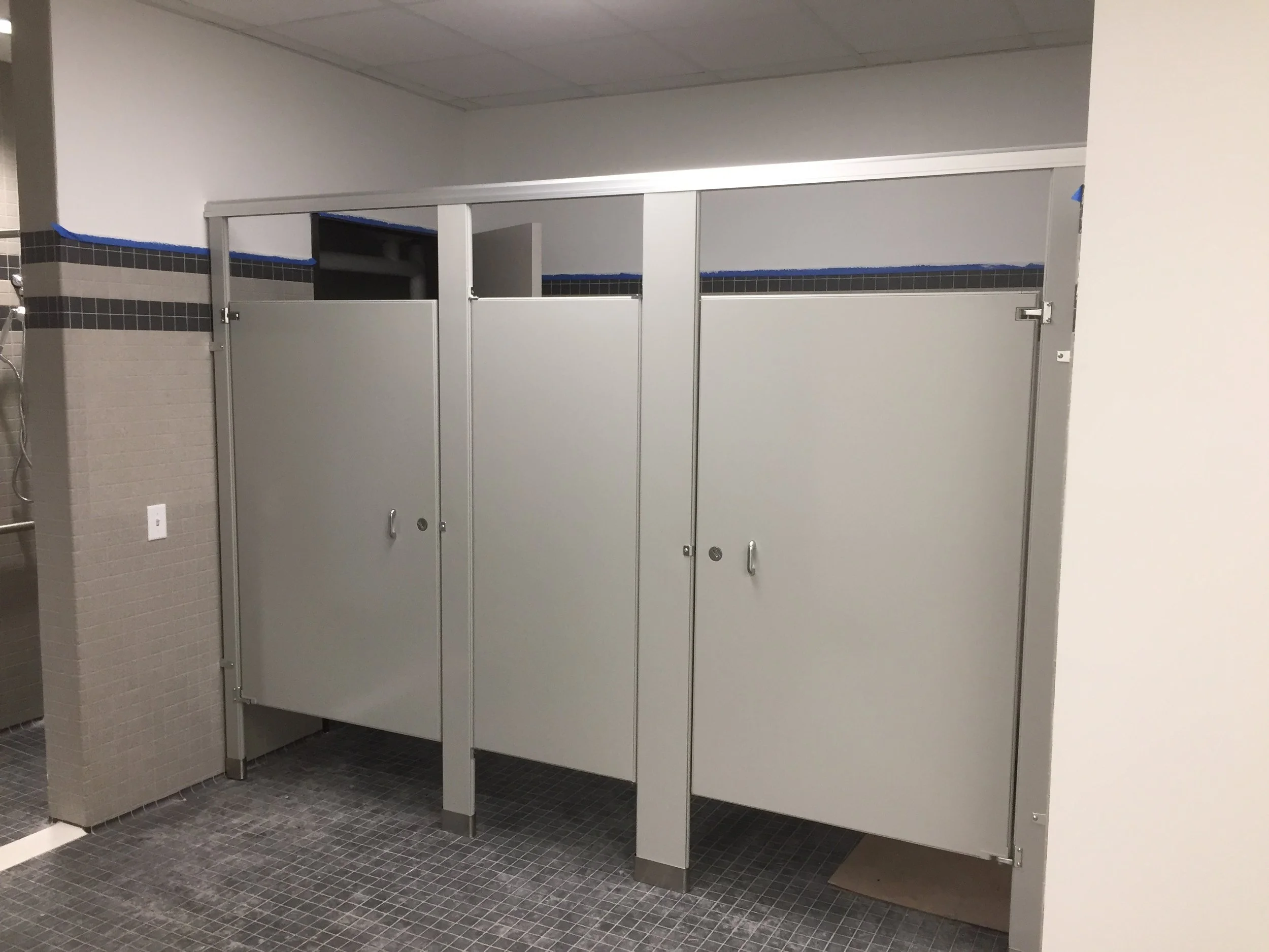 Public restroom with gray partition stalls and black tile accents on the upper walls.