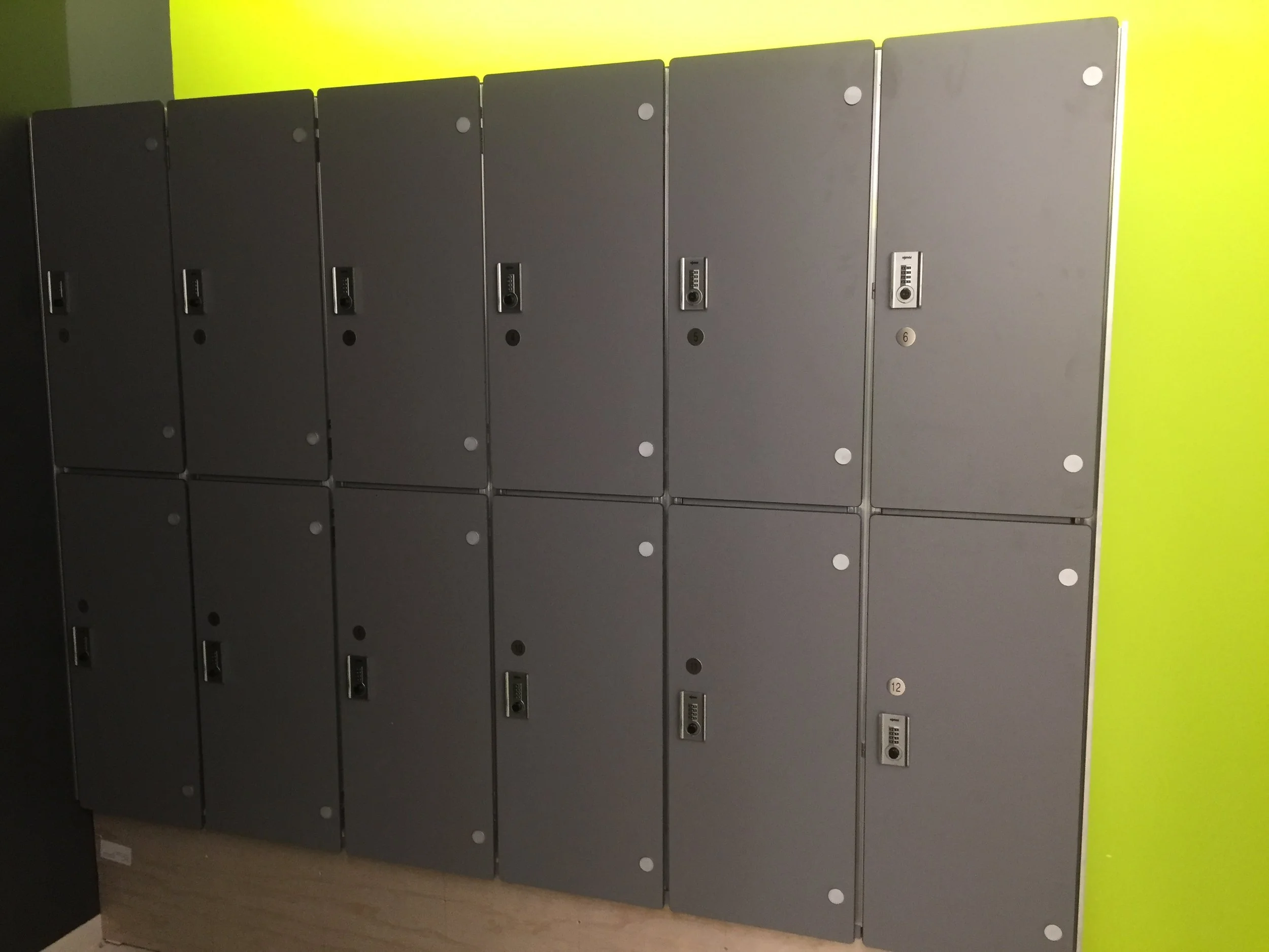 Row of gray lockers with combination locks, numbered from 1 to 12, against a yellow wall.