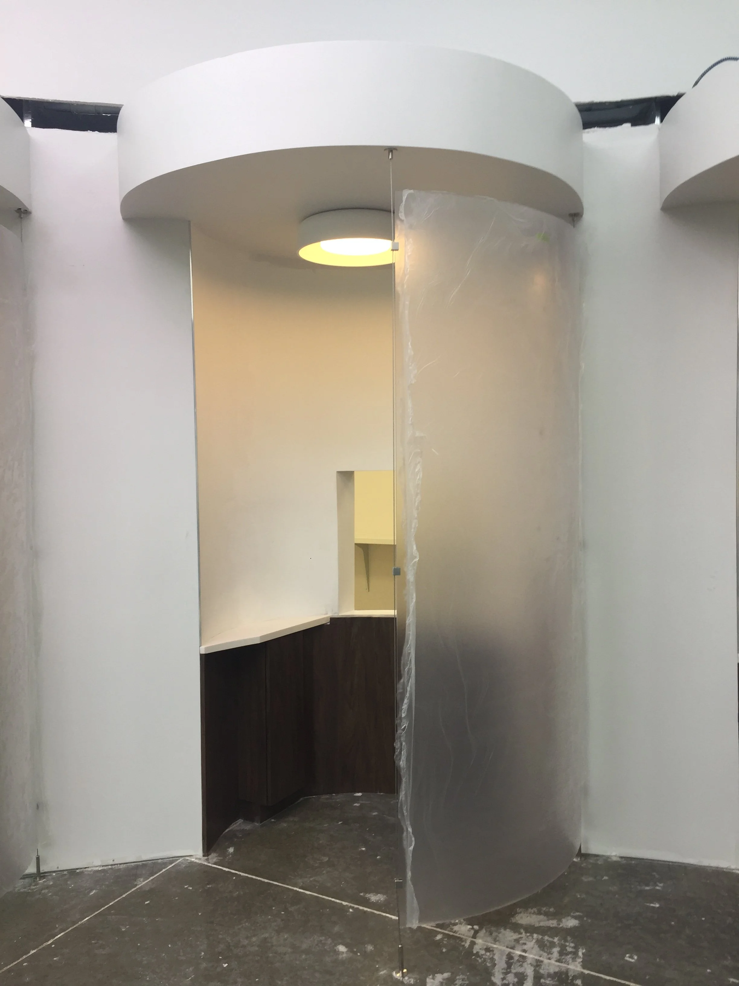 Modern interior space under construction with curved white walls and a round ceiling light.