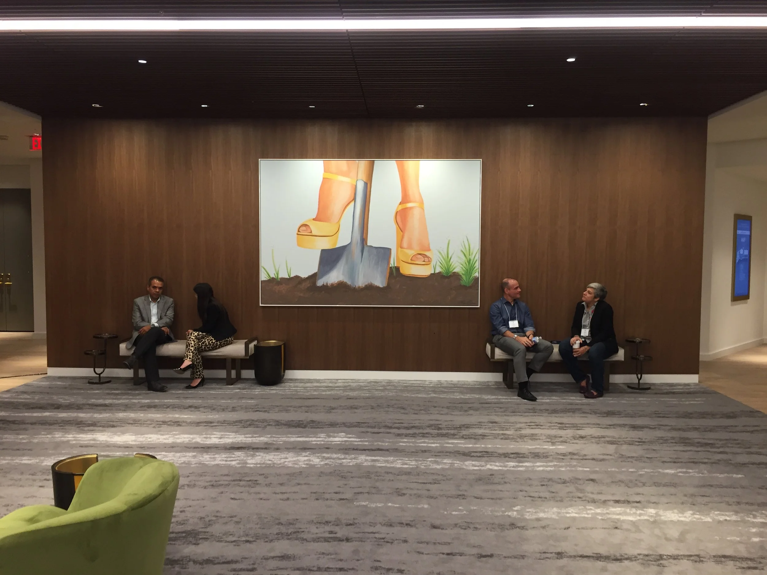 People sitting and talking in a lobby or waiting area with a large wall art featuring a giant open shoe and a shovel.