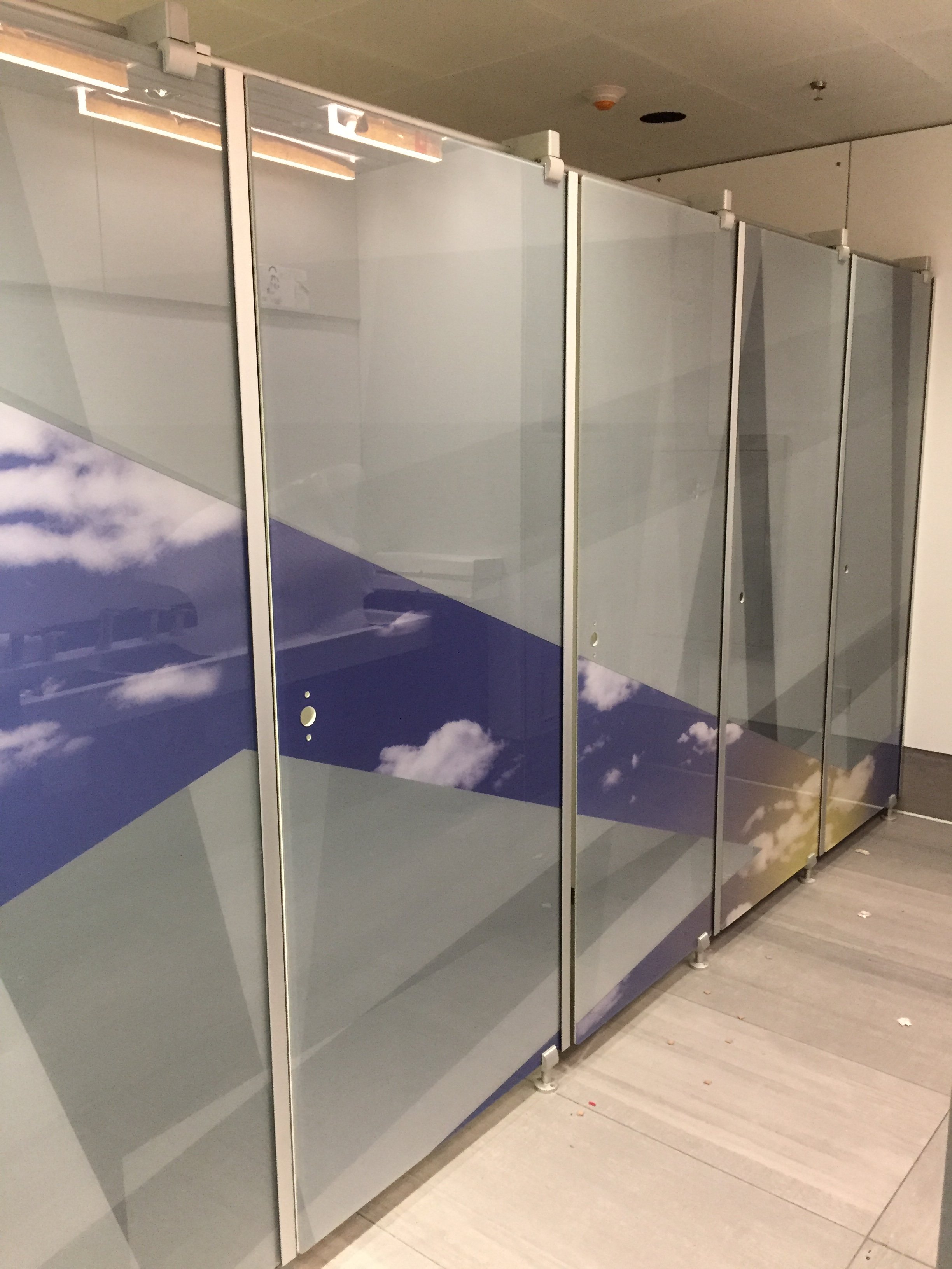 Public restroom stalls with blue sky and white clouds design on the doors.