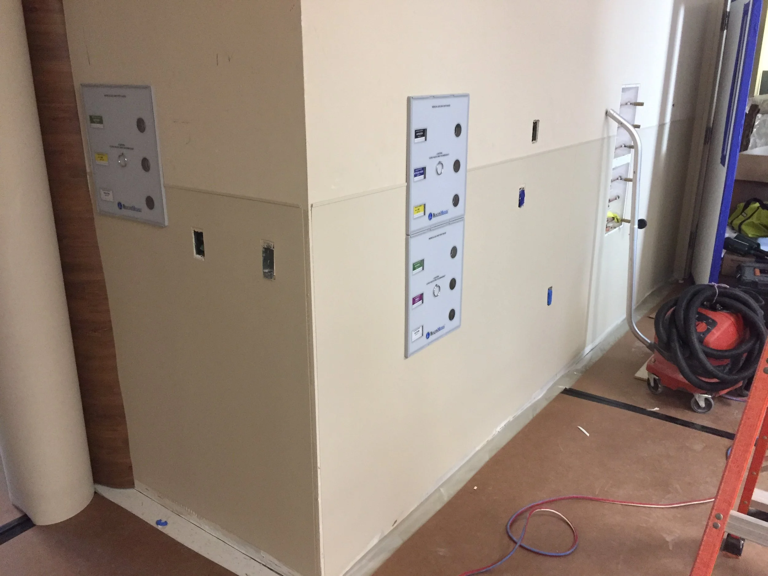 A large, beige electrical cabinet or panel with several access doors, located in an unfinished room with construction tools and materials nearby.