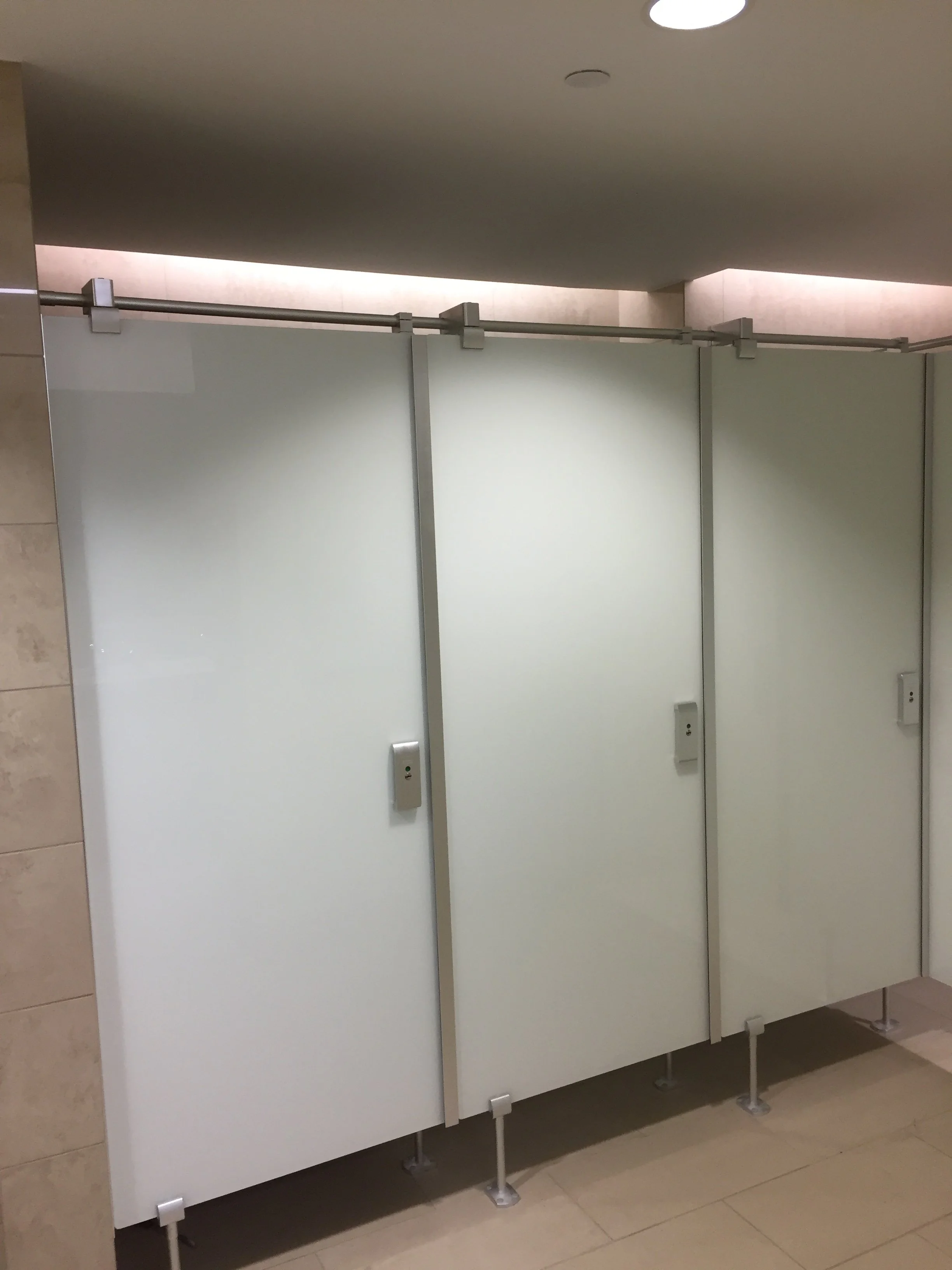 Public restroom stalls with closed doors, two electrical outlets, and a beige tiled floor.