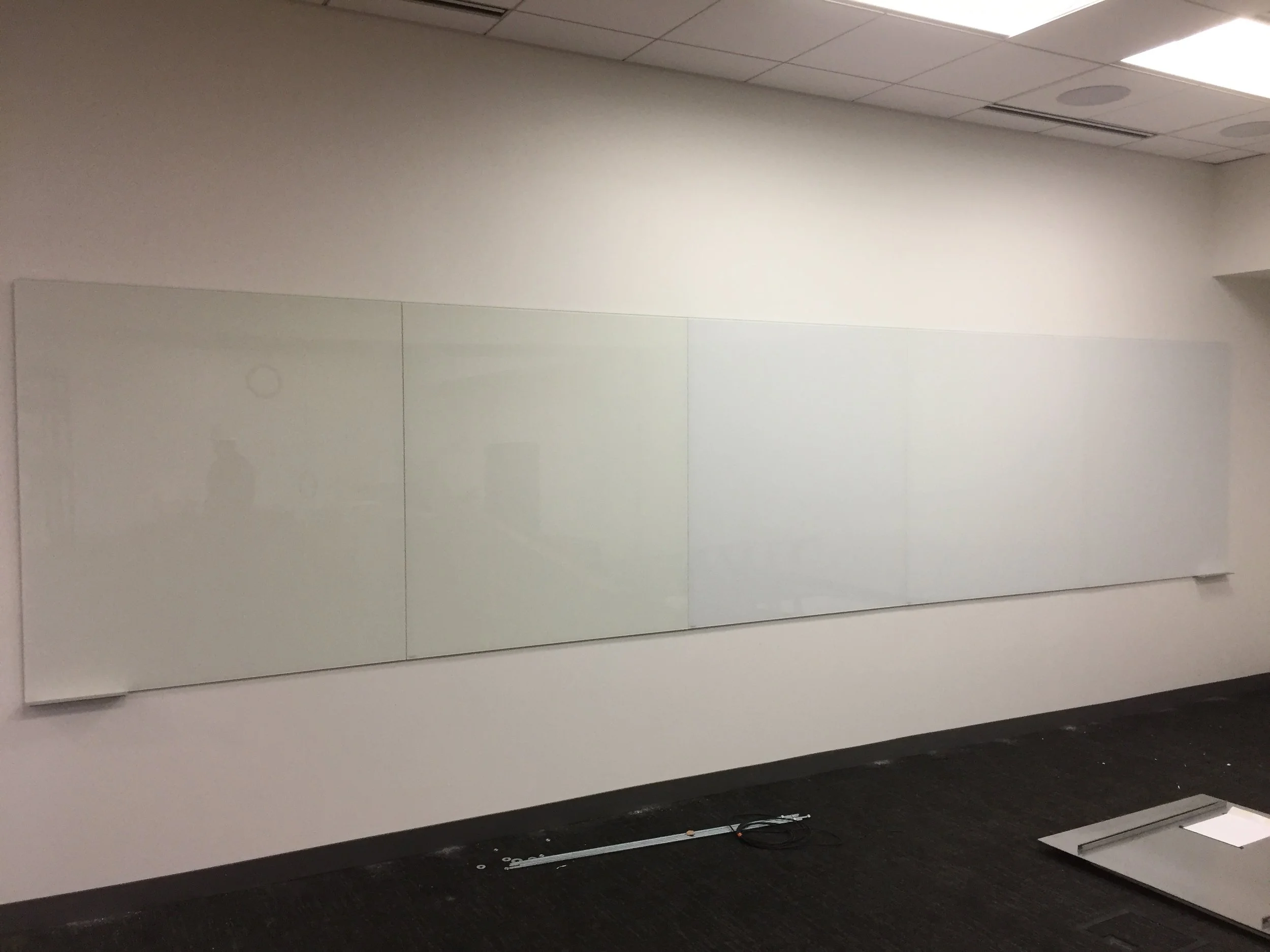 An empty whiteboard mounted on a wall in a classroom or conference room, with a black carpeted floor below.
