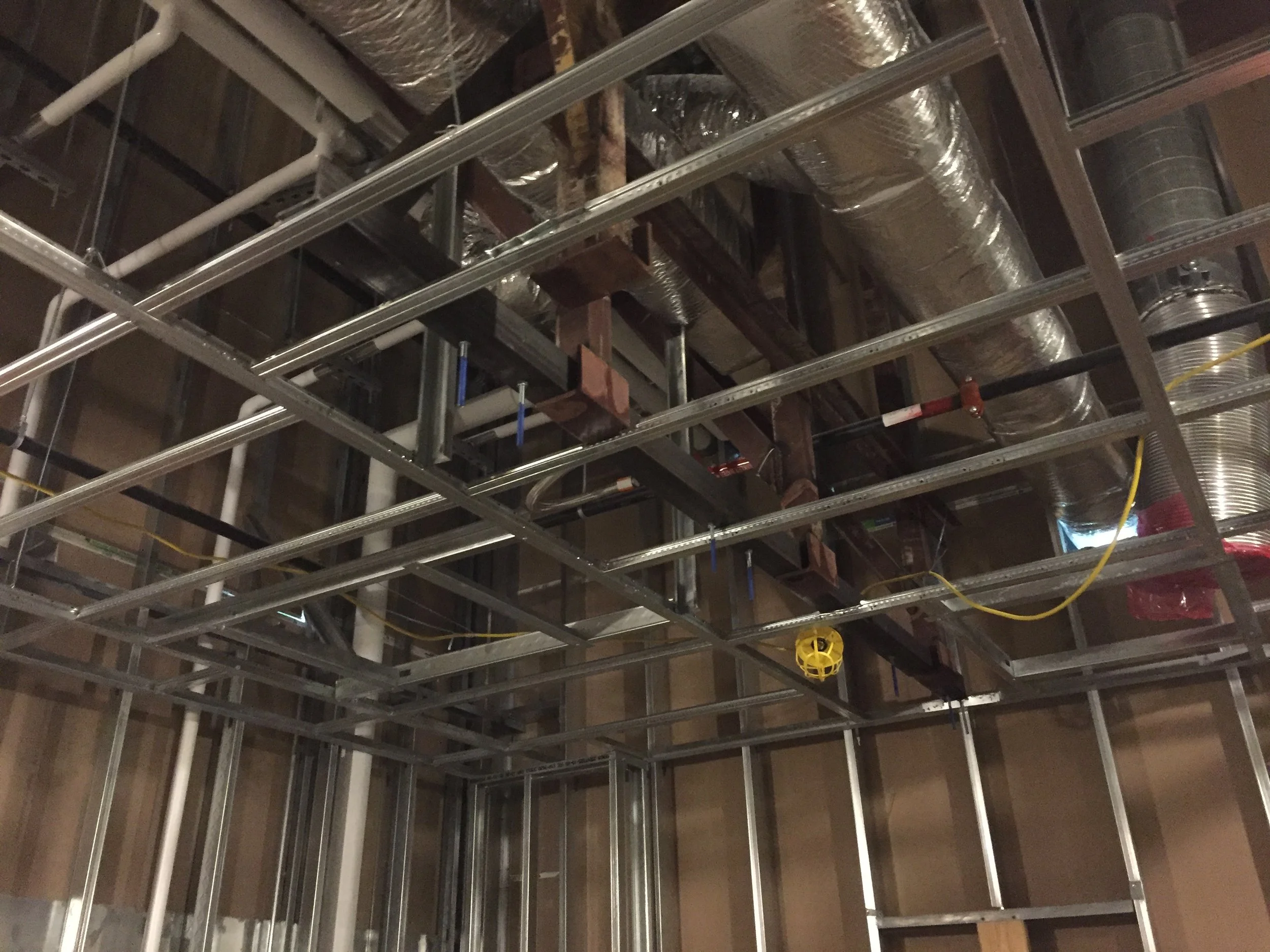 Construction framing with metal studs and ductwork overhead in an unfinished building interior.
