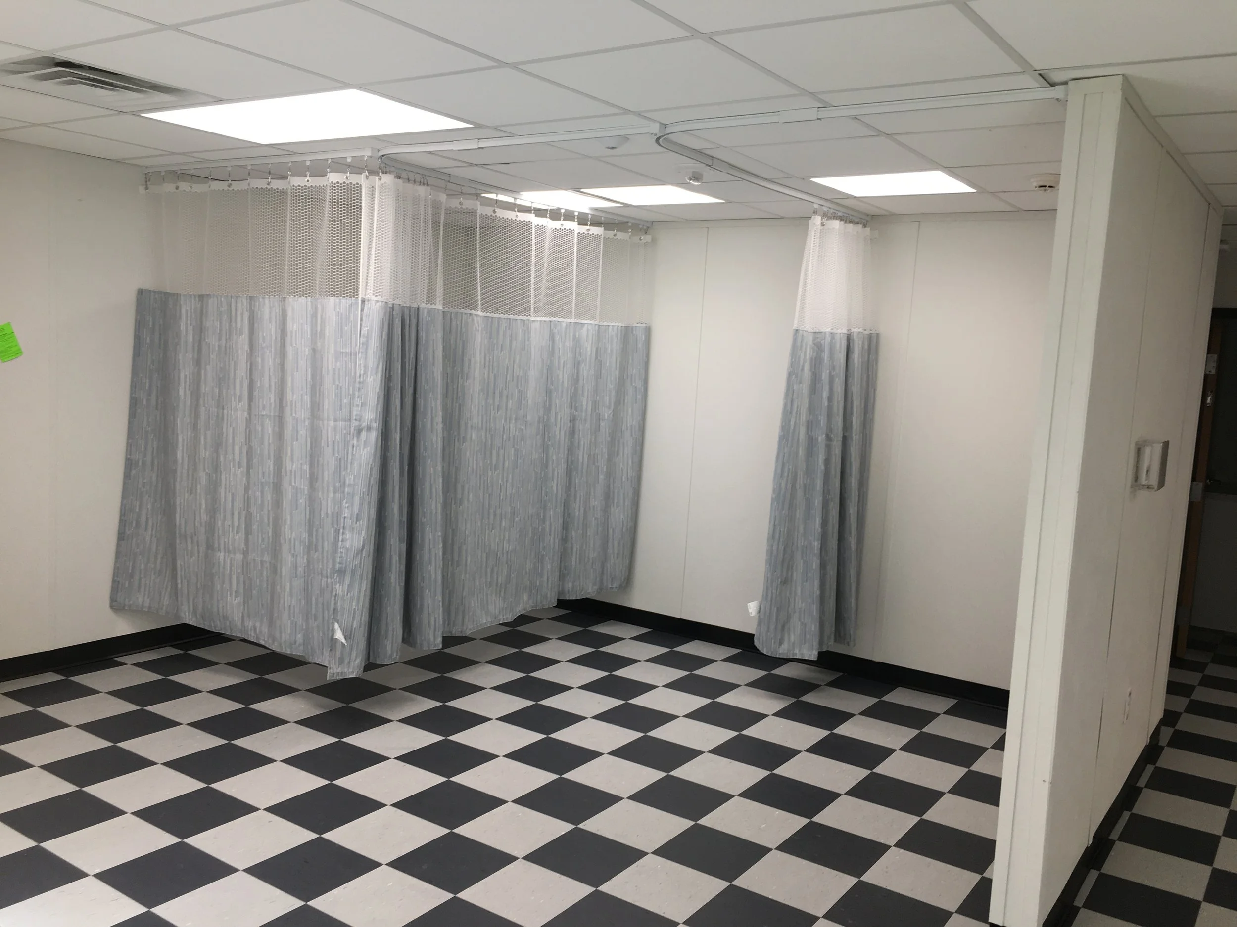 A vacant voting booth with curtains in a checkered black and white floor room, part of a polling station.