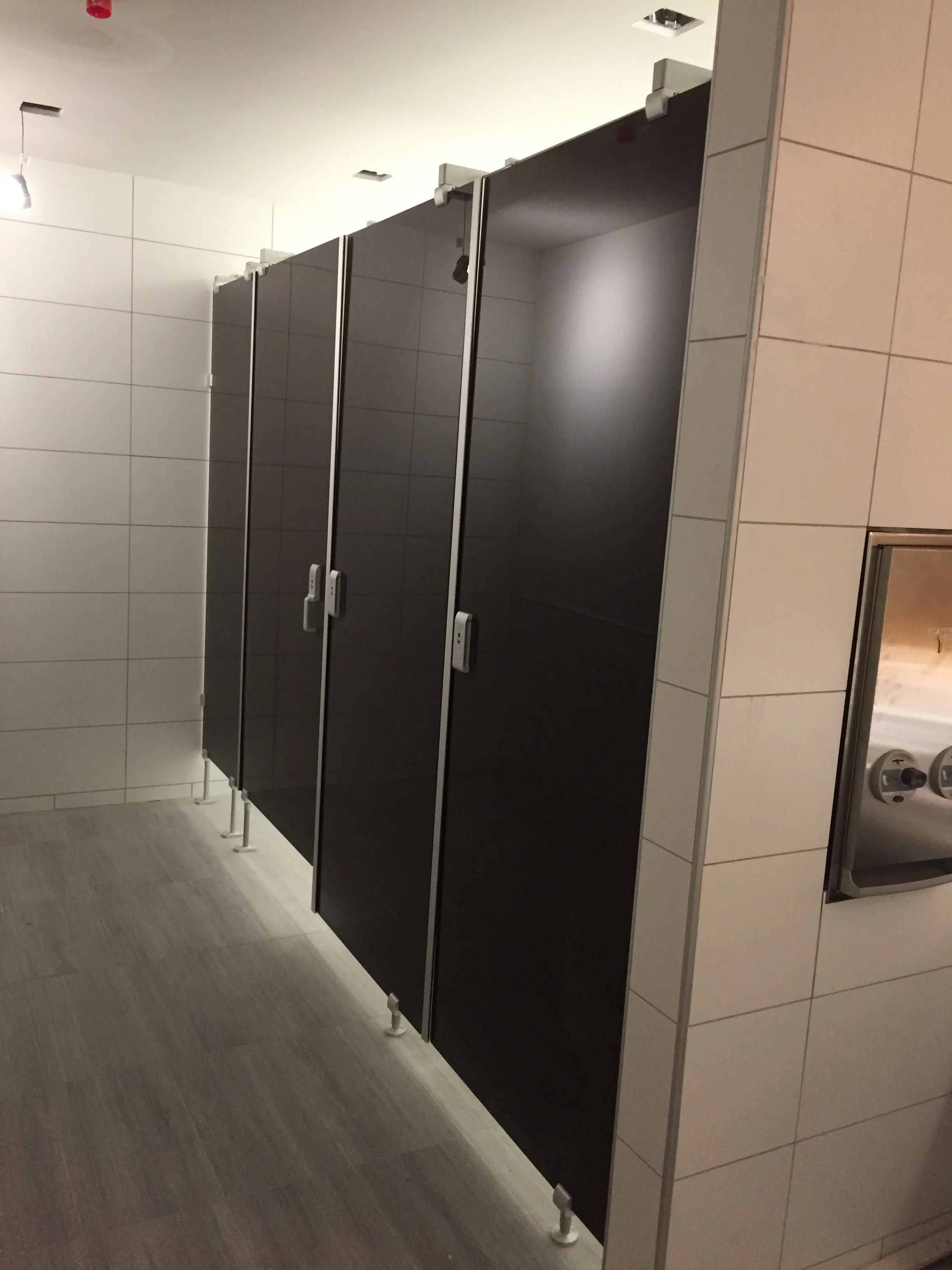 Public restroom with black stalls, white tile walls, and a sink area visible to the right.
